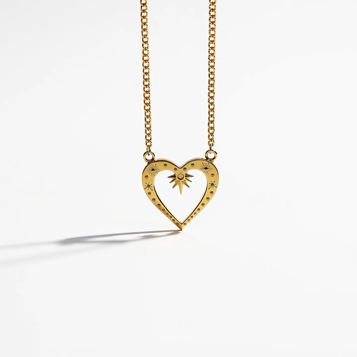 This heart chain necklace features a gold-toned metal heart pendant adorned with decorative engravings and a starburst design at its center. The pendant is connected to a chain on each side through small loops, emphasizing its symmetrical placement. The starburst design is highlighted by a small, circular gem at its core, set in a bezel setting that securely holds the gem in place. The necklace exhibits a classic cable chain, adding a traditional touch to the overall design. The clasp is not visible, suggesting a seamless look to the piece.