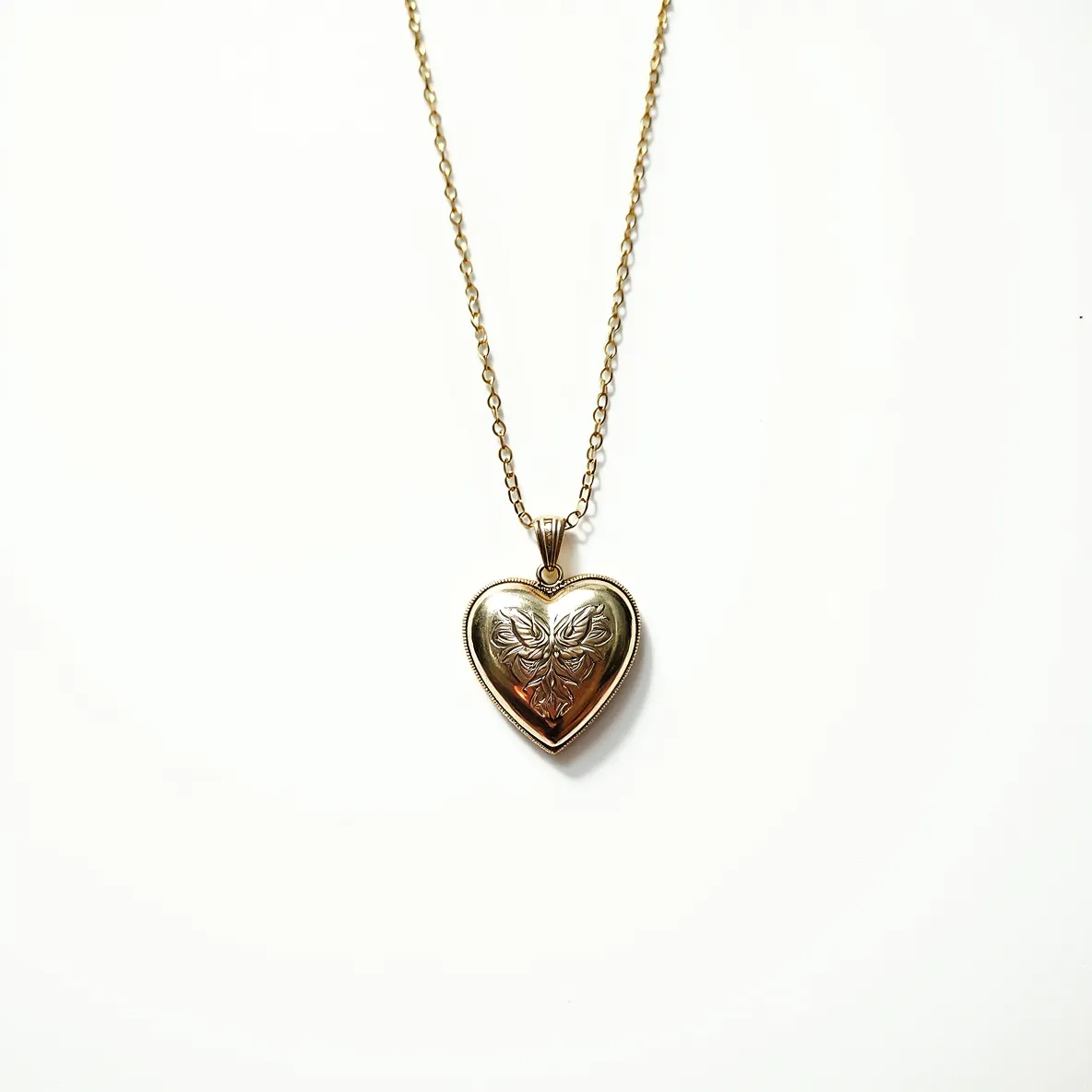 This heart locket features a golden appearance, showcasing a beautifully engraved design on the front that adds an elegant touch to its surface. The locket is attached to a delicate gold chain which complements its polished look. It includes a simple looped bale, providing a seamless connection between the chain and the locket. The subtle, intricate detailing on the locket enhances its vintage charm, making it a lovely keepsake or fashionable accessory.