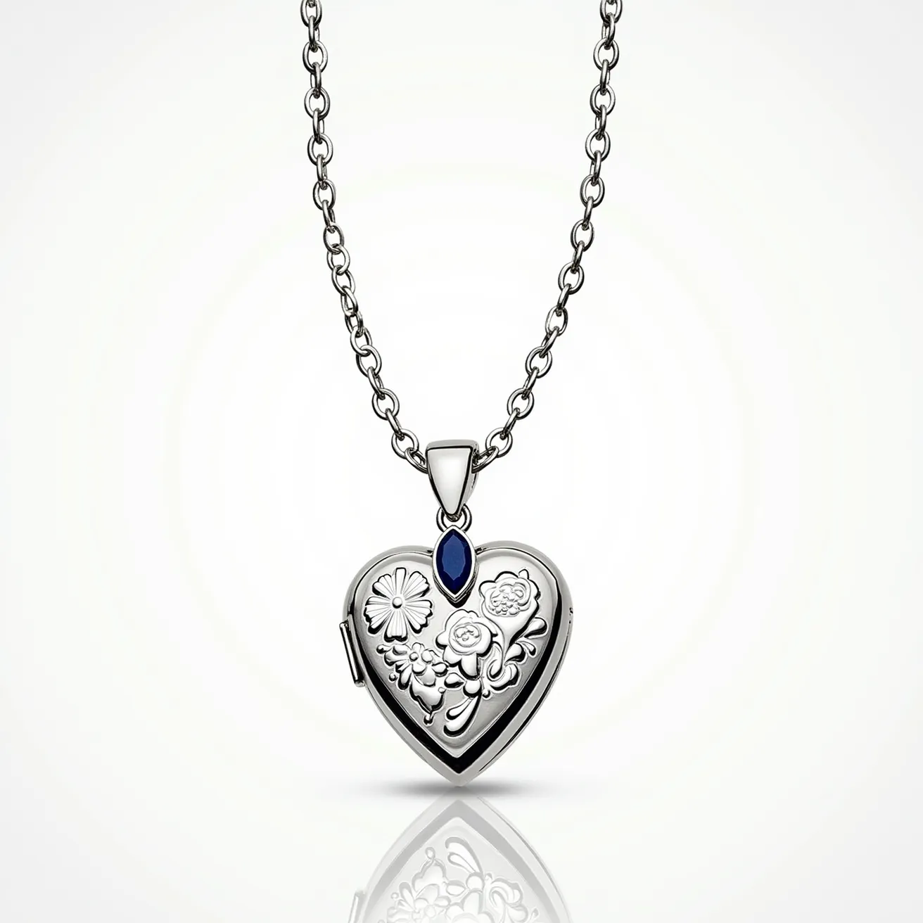 This heart locket is crafted from a shiny metal, likely silver or stainless steel, and features intricate floral engravings on its face. At the top center of the locket, there is a marquise-cut blue gem, possibly a sapphire or blue topaz, securely set within a simple bezel setting. The locket hangs from a matching metal chain with a series of interconnected oval links, which attaches to the locket via a prominent bail. The overall design is elegant yet understated, making it suitable for a variety of occasions.