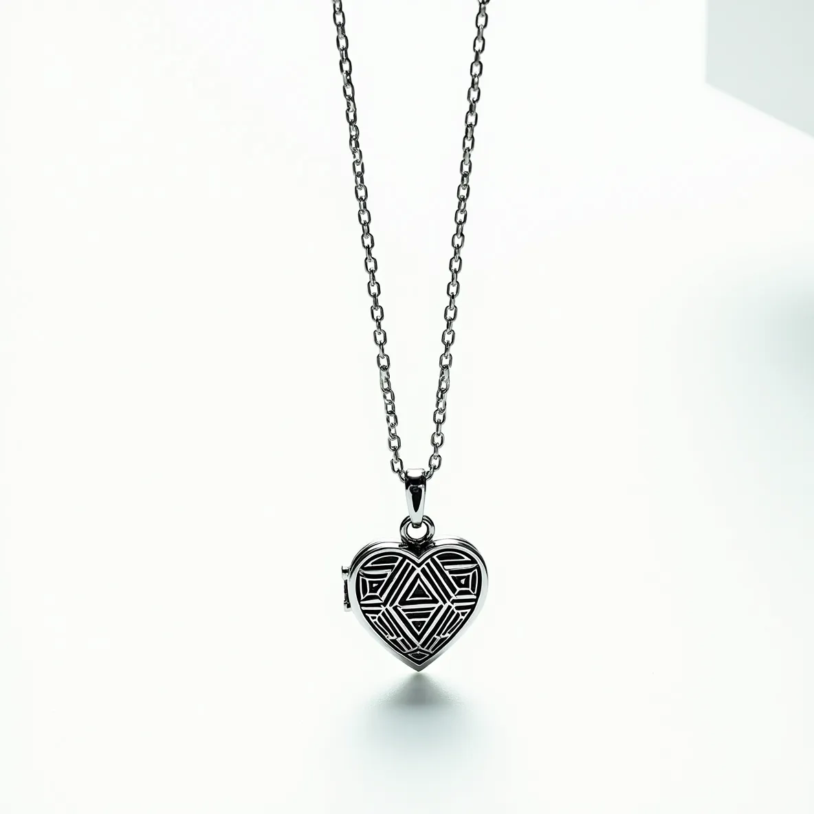 This heart locket is crafted from a shiny metal, likely silver or a silver-toned material, giving it a polished and elegant appearance. The surface features an intricately patterned design that adds depth and character to its exterior. The locket is suspended from a matching chain, which has a series of evenly spaced links, providing a classic and durable attachment. The clasp at the top of the locket allows it to be easily attached or detached from the chain, offering practical versatility for the wearer.