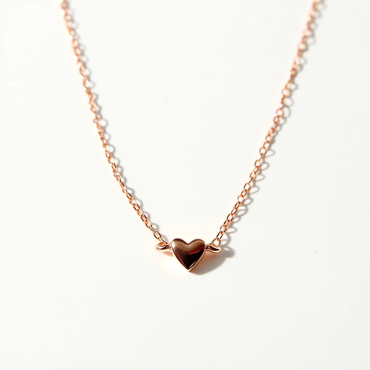 This heart necklace features a delicate chain made from a rose gold-toned metal, highlighting its elegant and minimalistic design. At its center lies a smooth, polished heart charm, giving the piece a subtle yet sophisticated touch. The heart is flanked by small, stylized wings adding a unique flair to the design. The necklace is likely secured with a typical lobster claw clasp, ensuring it stays comfortably in place while worn. The simplicity and charm of this piece make it a versatile accessory suitable for various occasions.