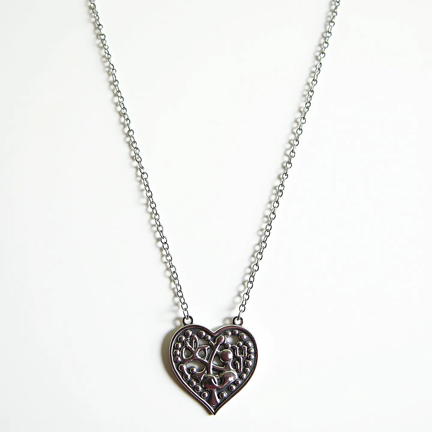 This heart necklace features a metallic heart-shaped pendant with an intricate, raised design that includes various shapes and patterns, giving it an ornate, almost vintage appearance. The pendant is suspended from a slender chain composed of small, uniform links, likely made from silver or a similar metal, providing a sleek and elegant look. The metal used in the design appears to have a polished finish, enhancing its visual appeal. There are no visible gems or stones embedded within the pendant, allowing the detailed metalwork to be the focal point. The necklace likely includes a standard clasp mechanism for ease of wear.