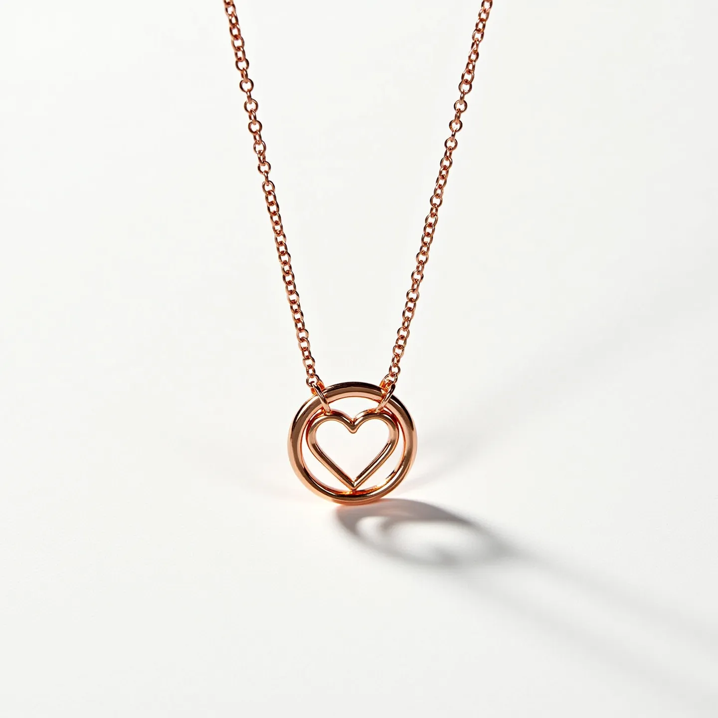 This heart necklace features a simple yet elegant design crafted from rose gold-colored metal. The pendant consists of a delicate heart shape nestled within a perfect circle, both seamlessly integrated, creating a harmonious and fluid design. The necklace is suspended on a fine chain that connects to the pendant through two small loops at the top of the circle. There are no visible gemstones or elaborate settings, keeping the focus on the understated beauty of the metalwork. The necklace likely uses a standard clasp mechanism to secure it around the neck, enhancing its practicality.