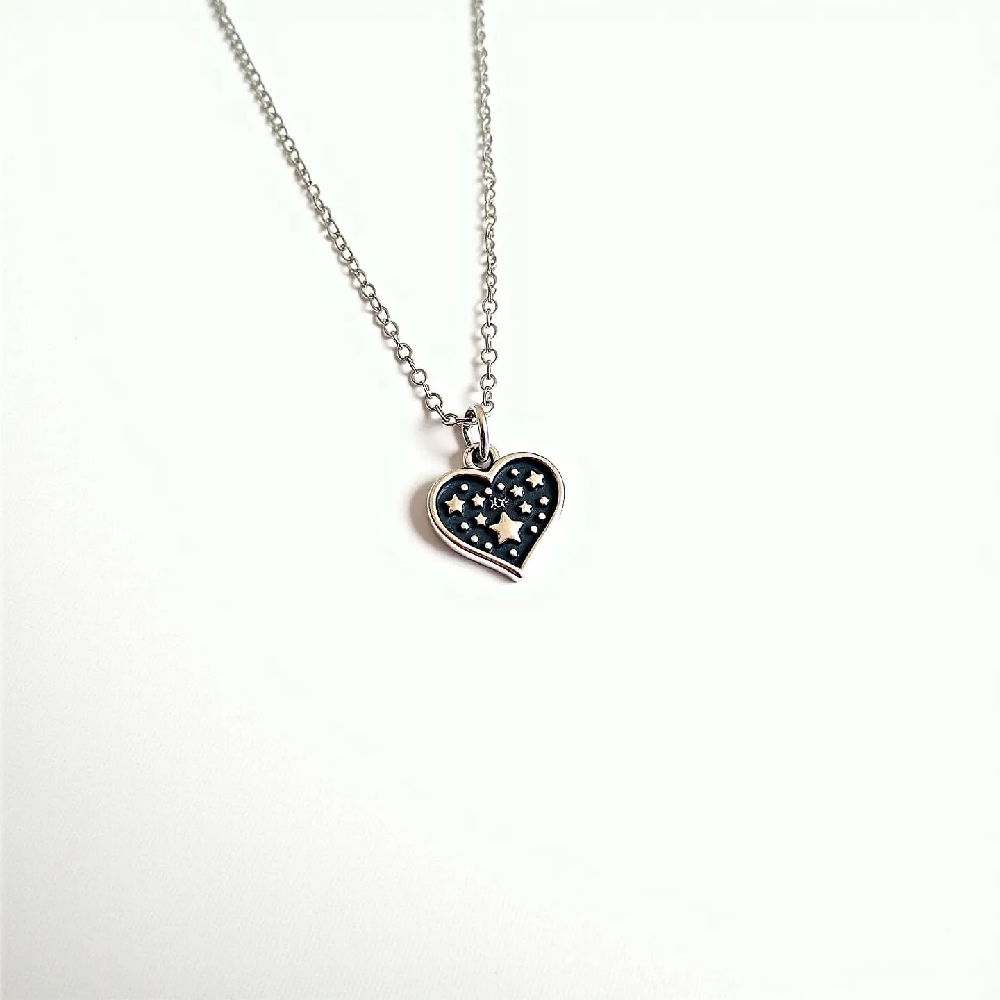 This heart necklace features a delicate design with a chain that appears to be made of silver or a similar metal, lending a sleek and elegant appearance. The pendant is heart-shaped, adorned with a series of star-like embellishments against a dark background, which may give the impression of a nighttime sky. The stars are likely also crafted from metal, possibly the same material as the chain, enhancing the unity of the design. The heart pendant is attached to the chain with a small loop, providing a simple yet secure connection. The chain is a classic cable style, allowing for flexibility and ease of wear, while the clasp, not visible in the image, is likely a standard lobster or spring ring for reliability.