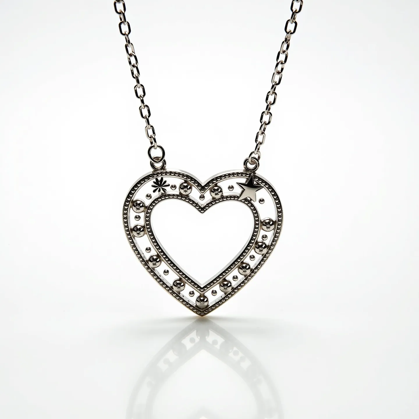 This heart necklace features an open-heart design crafted from what appears to be a silver-toned metal. The pendant is adorned with various small metal embellishments, including a star and round studs, which contribute to its decorative pattern. The heart is outlined by a row of small, evenly spaced beaded details, adding texture and depth to its appearance. The pendant is attached to a chain via two small loops, one on each of the upper curves of the heart. The chain itself consists of uniformly sized oval links, completing the elegant and stylish design of the necklace.