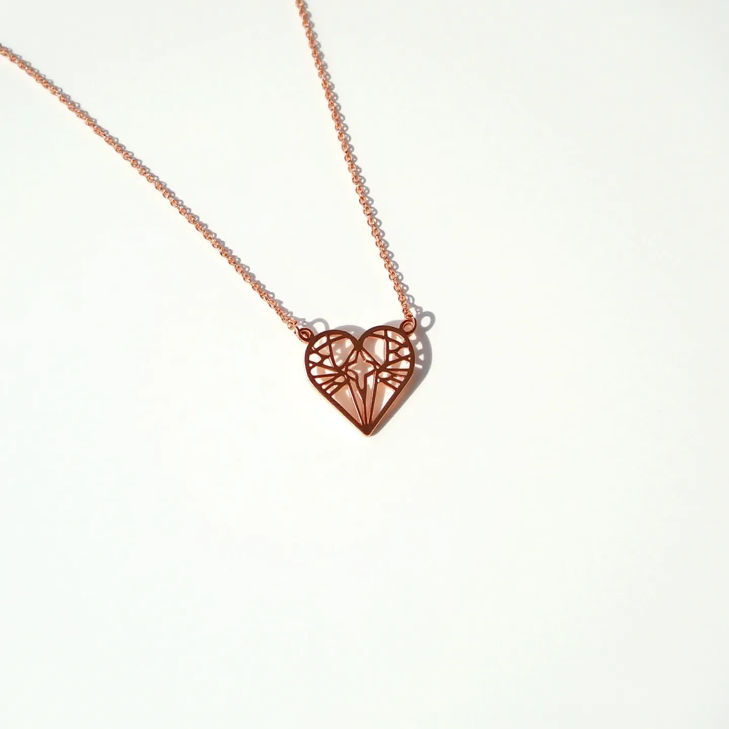 This heart necklace features a delicate rose gold-toned metal design, forming an open-work heart shape with an intricate geometric pattern. The pendant is attached to a fine matching chain that enhances its elegance. While the necklace does not appear to include any gemstones, its minimalist and artistic construction adds a unique charm. The heart pendant is securely connected to the chain with small loops, ensuring stability. This beautifully crafted piece exudes simplicity and sophistication, suitable for everyday wear or special occasions.