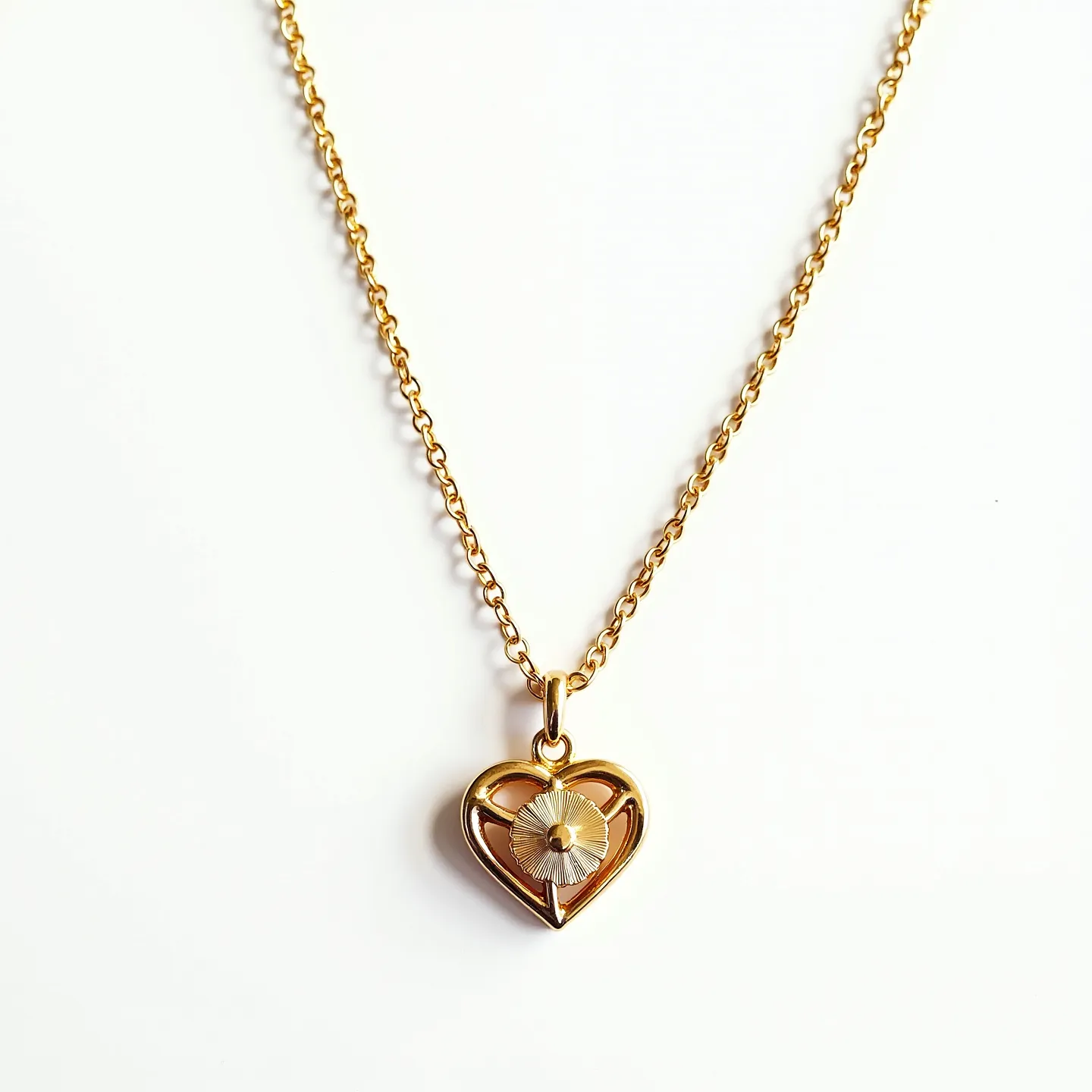 This heart necklace features a gold-tone chain with a delicate, openwork heart pendant. Within the heart design, there's an intricate floral motif that seems to be crafted in a contrasting metallic shade, possibly silver, with a textured disc and a small central bead suggestive of a flower. The pendant is connected to the chain by a simple gold-tone bail. The chain appears to have a classic cable link pattern, known for its interlocking oval links, likely secured with a conventional spring ring clasp. The combination of gold tones and floral detailing gives the necklace an elegant and timeless appeal.