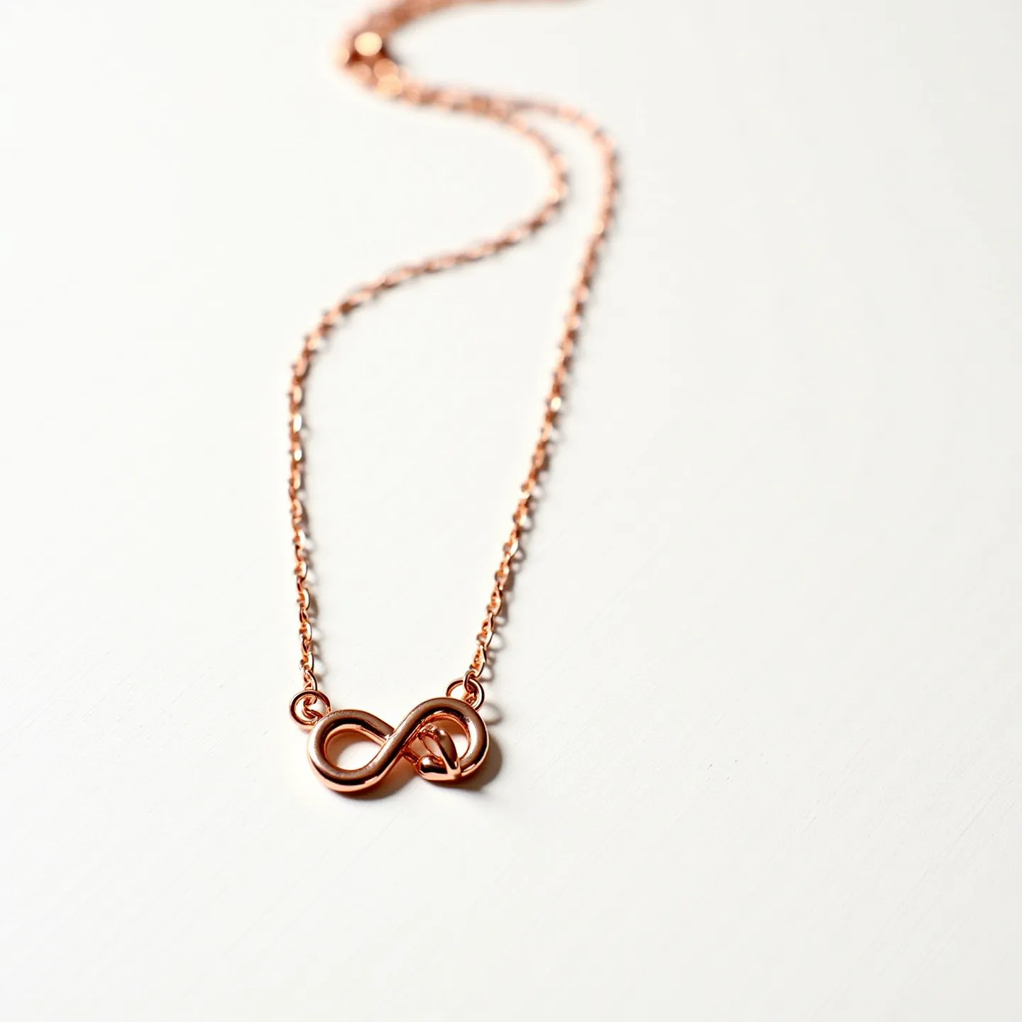 This infinity heart necklace features a delicate rose gold chain with an infinity symbol integrated with a heart motif at its center. The pendant is crafted from a lustrous rose gold metal, adding a warm and elegant touch to the piece. The necklace is equipped with a standard lobster clasp, which provides secure fastening. The design is simplistic yet stylish, making it a versatile accessory suitable for various occasions.