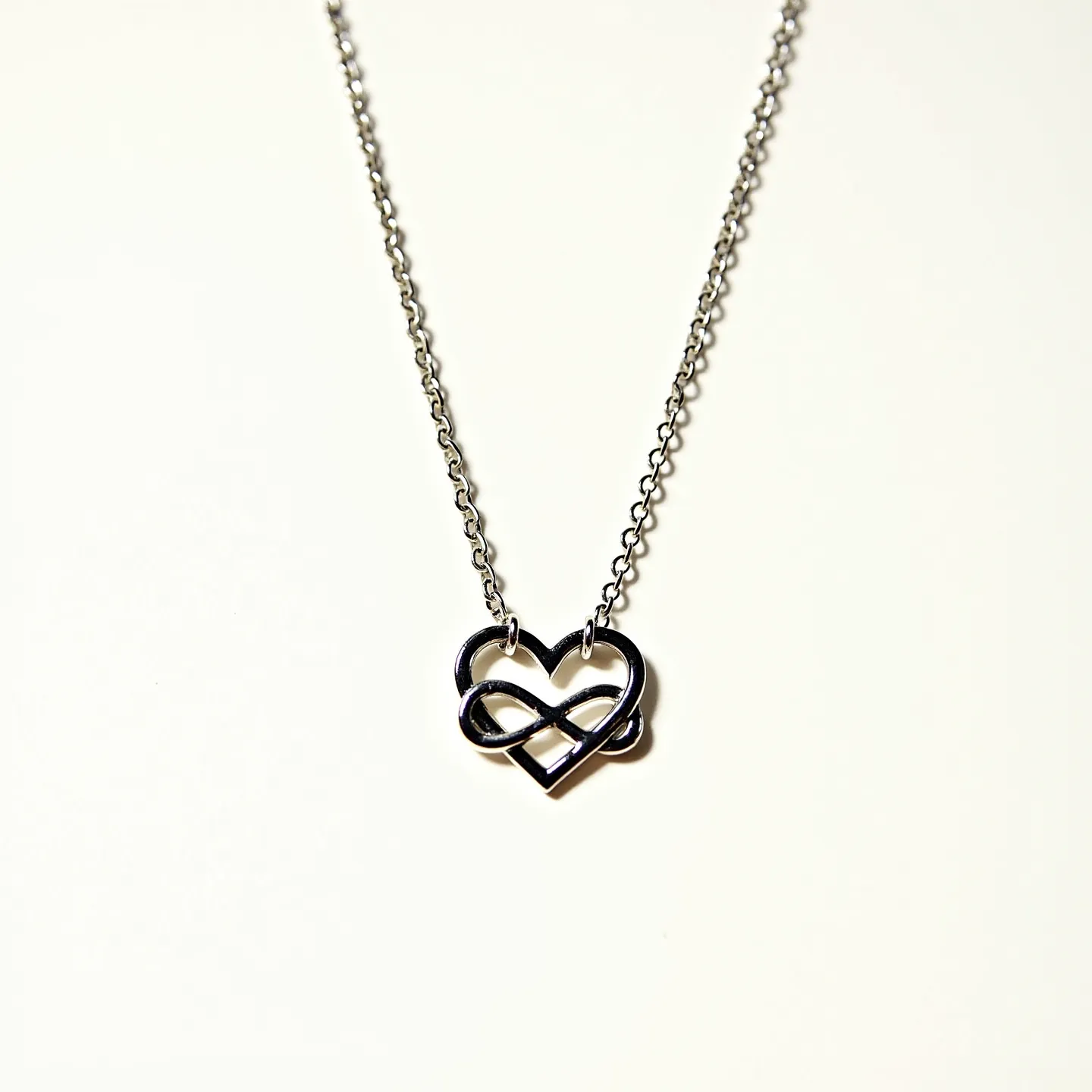 This infinity heart necklace features a sleek design crafted from polished metal, forming an interwoven infinity symbol within a heart shape. The pendant is suspended from a delicate chain that complements the pendant's simplicity. The necklace is likely to have a spring ring clasp, ensuring a secure and comfortable fit. The minimalist design highlights the elegant flow of the intertwined shapes, creating a harmonious balance between modernity and sentimentality.