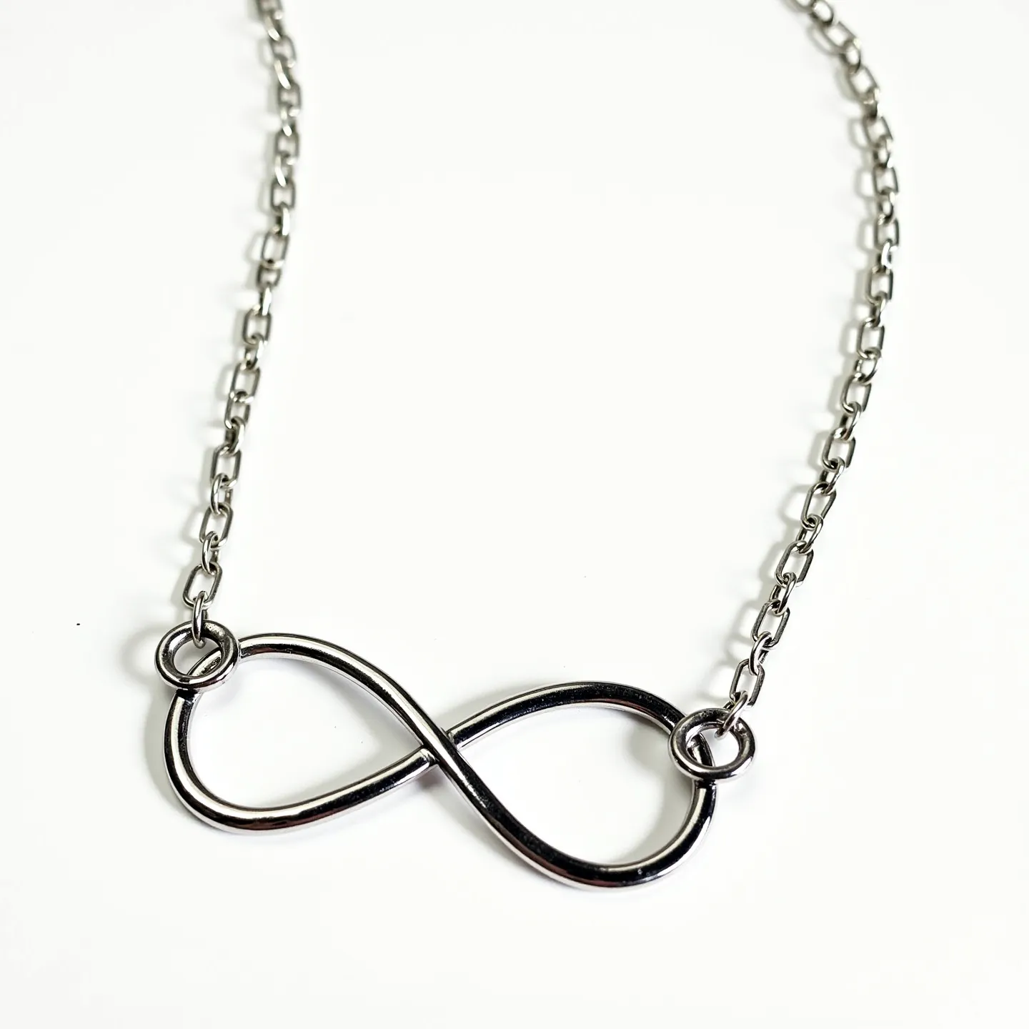 This infinity necklace features a sleek metal design, likely made from sterling silver or stainless steel, given its polished and reflective surface. The infinity symbol is smoothly crafted without any additional adornments such as gems, giving it an elegant simplicity. It is attached to a delicate chain via two small, secure rings at each end of the symbol, ensuring durability and aesthetic balance. The chain links are oval-shaped, providing a classic look that complements the pendant well. The necklace is likely secured with a simple clasp at the back, typical for necklaces of this style, to allow easy fastening and removal.