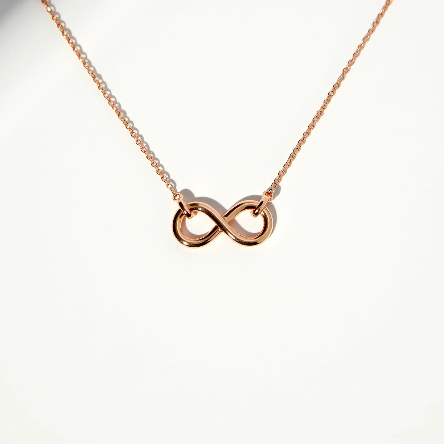 This infinity necklace features a minimalistic design, crafted from what appears to be rose gold metal, giving it a warm and elegant finish. The infinity symbol is smoothly polished, creating a sleek, continuous loop that is both modern and timeless. The pendant is delicately attached to a fine chain, ensuring the focus remains on the symbolic centerpiece. The chain likely has a simple clasp, which is common for such elegant pieces, ensuring both security and ease of use. This necklace exemplifies understated sophistication, suitable for a variety of occasions.