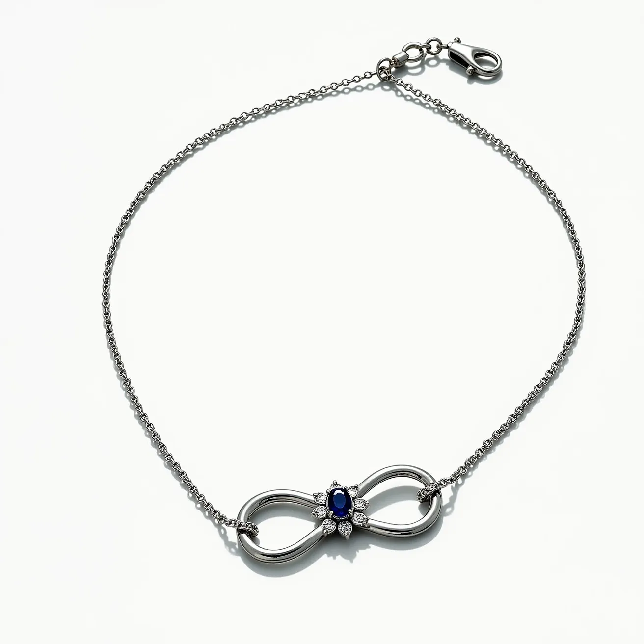 This infinity necklace features a polished metal chain and pendant, showcasing a central oval blue gem. The gem is encircled by a series of small clear stones arranged symmetrically on either side, enhancing its elegance. The stones are likely set in a prong setting that secures them in place while allowing maximum light to pass through. A lobster clasp attaches to small rings at the end of the chain, ensuring a secure fit around the neck. The overall design combines simplicity and sophistication, with the infinity symbol serving as a timeless motif.