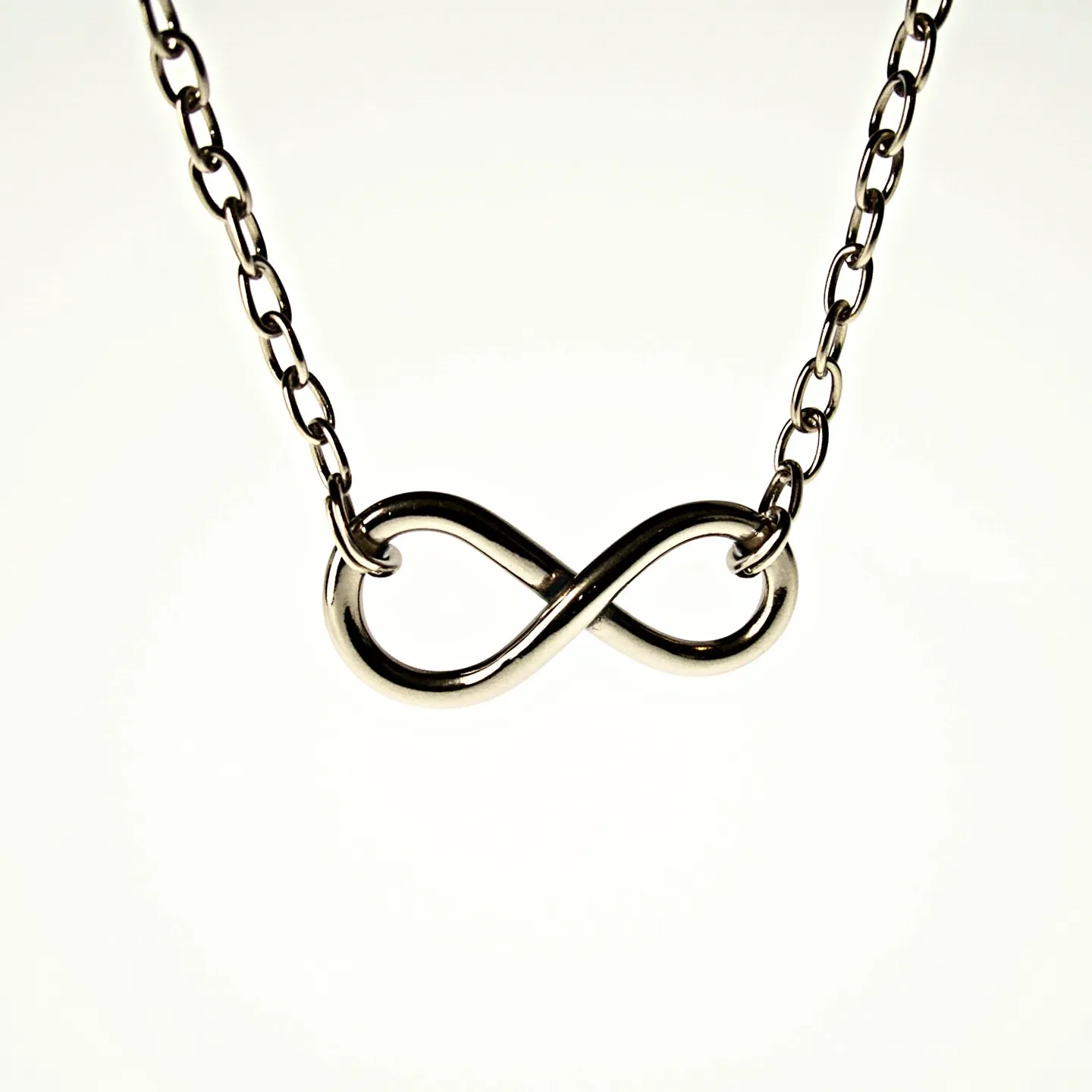 This infinity necklace features a sleek, polished metal infinity symbol as its central pendant. The symbol seamlessly connects to a classic chain composed of uniform, oval links, adding to its minimalist elegance. The metal has a shiny finish, indicative of stainless steel or possibly sterling silver. The necklace is likely equipped with a simple clasp mechanism, typical of such designs, though the exact type is not visible. The overall aesthetic of the necklace offers a timeless design, emphasizing the continuity and balance of the infinity motif.