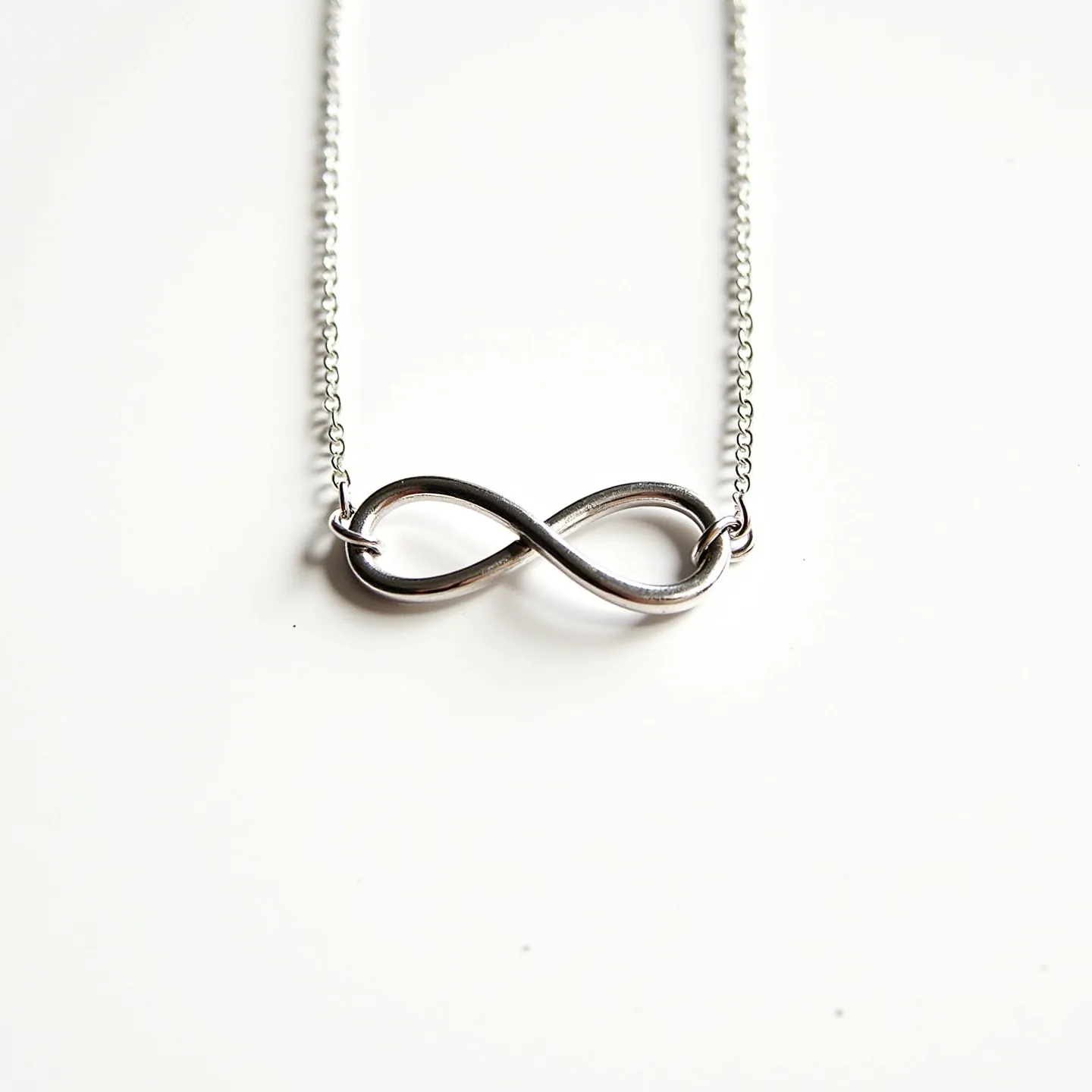 This infinity necklace features a sleek and elegant design with a polished silver-tone infinity symbol at its center. The infinity pendant is seamlessly integrated into the necklace, with a delicate chain that enhances its minimalist appeal. The chain appears to be crafted from a fine metal, possibly sterling silver, providing a subtle sheen that complements the pendant. The necklace likely includes a small, discreet clasp, such as a lobster or spring ring, for secure attachment. Overall, its refined simplicity makes it a versatile accessory suitable for various occasions.