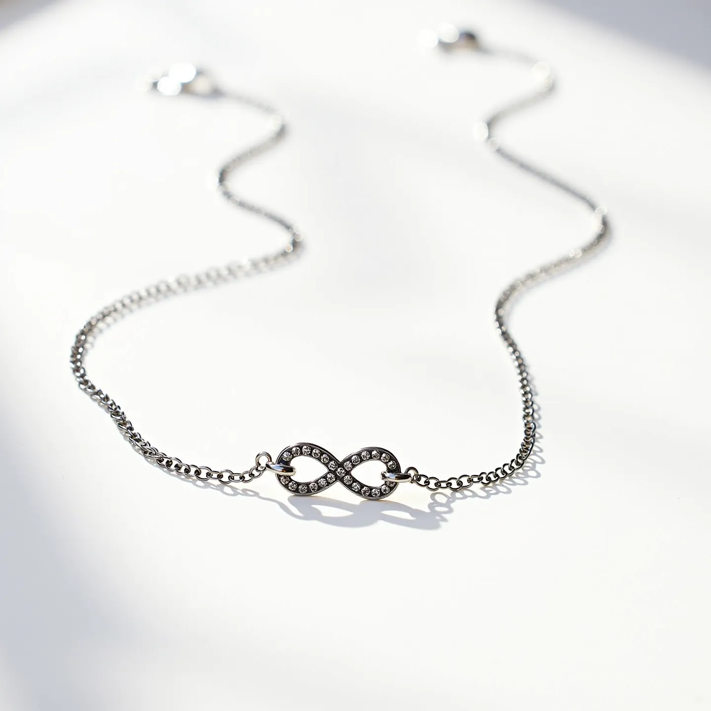 This infinity necklace features a delicate chain crafted from a silver-toned metal, giving it a sleek and elegant appearance. The centerpiece showcases an infinity symbol adorned with small, round-cut clear stones, likely cubic zirconia or diamonds, set close together to enhance their sparkle. The stones are set in a classic pavé style, which adds to the necklace's refined look. The necklace is equipped with a subtle, secure clasp that ensures it stays fastened when worn, making it both beautiful and practical for daily wear or special occasions.