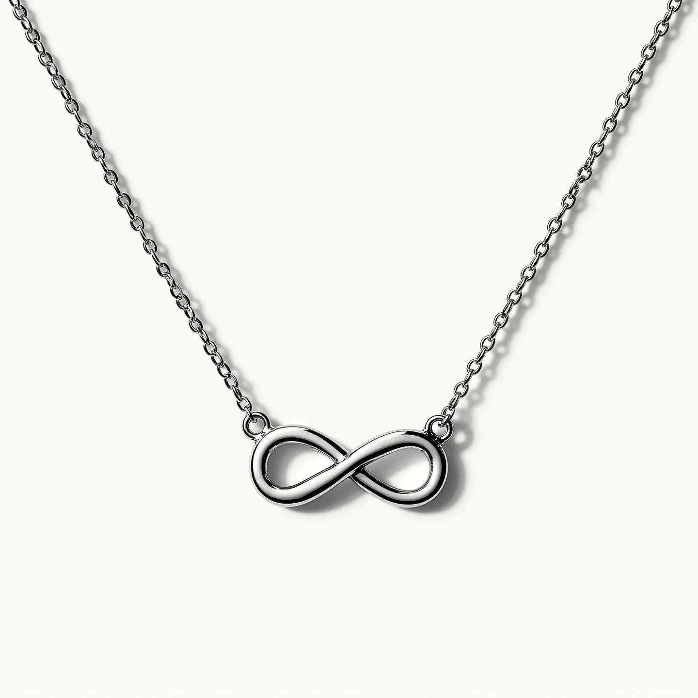 This infinity necklace features a sleek, polished infinity symbol crafted from a lustrous metal, likely silver or white gold, given its reflective quality. The charm is seamlessly connected to a delicate chain that enhances its elegant design. The chain appears to be a cable chain, known for its strength and simplicity, which complements the graceful form of the infinity charm. The necklace is equipped with a standard spring ring clasp, ensuring security and ease of wear. The overall design is minimalistic yet sophisticated, exuding a timeless appeal.