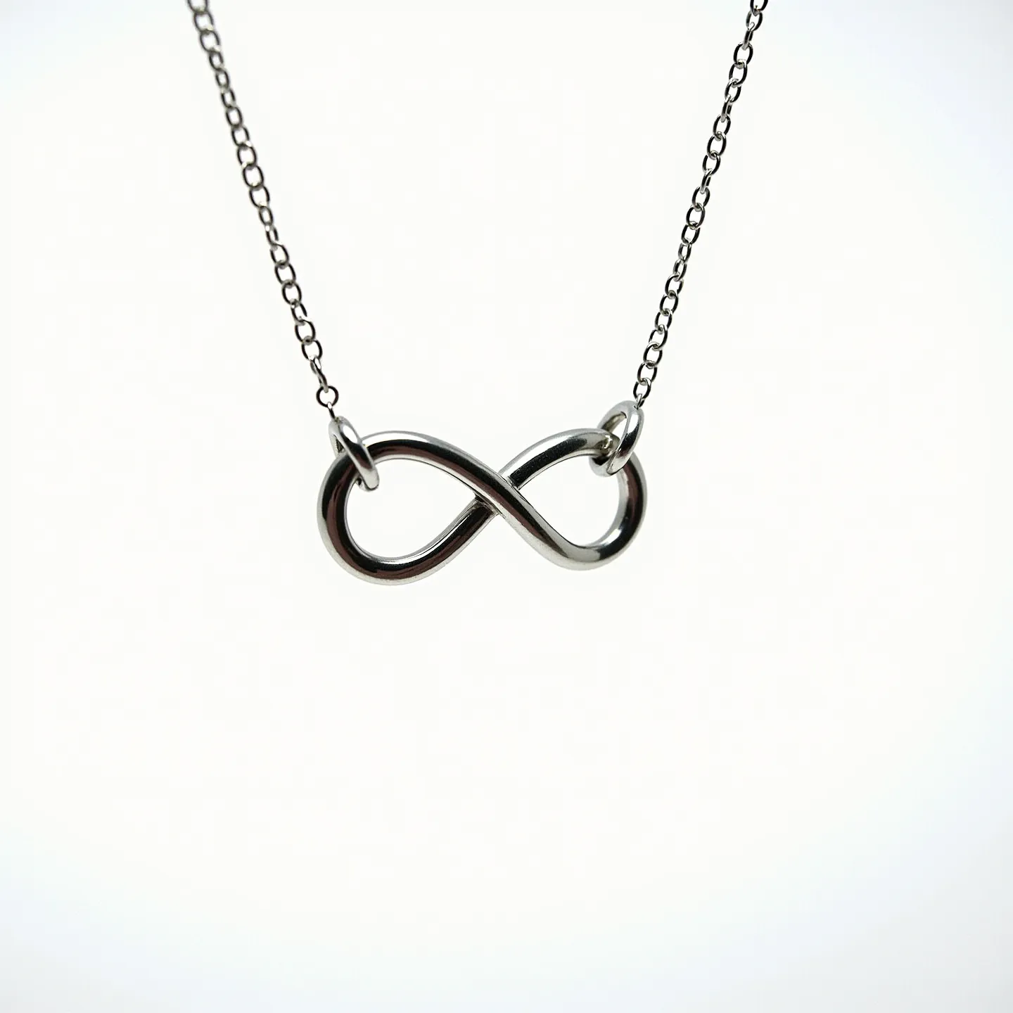 This infinity necklace features a sleek design with a polished metallic infinity symbol as its centerpiece. The symbol is elegantly crafted, showcasing a smooth, continuous loop with a lustrous finish, likely made from stainless steel or sterling silver. The necklace is attached by a delicate chain, secured by small loops at each end of the infinity symbol. The chain appears to be of a fine cable style, offering an understated complement to the central motif. A standard clasp likely secures the necklace, though the clasp is not prominently displayed in the image. This piece exudes a minimalist charm, making it a versatile accessory for various occasions.