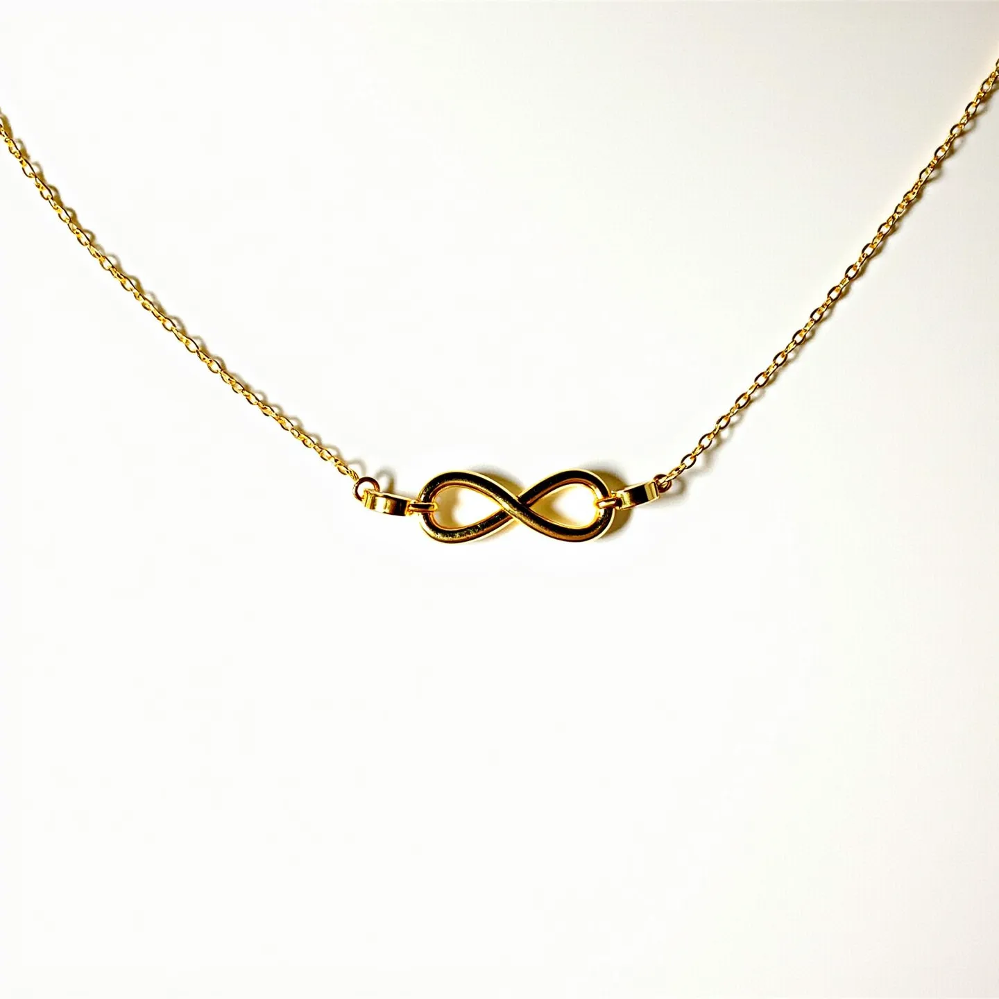 This infinity necklace features a sleek and polished infinity symbol crafted from a shiny gold-toned material. It is elegantly suspended on a delicate chain that matches the golden hue, highlighting its minimalist yet sophisticated design. The infinity charm is integrated seamlessly into the chain, which is secured by small connecting rings. The minimalist style of this necklace suggests a simple yet timeless elegance, making it versatile for various occasions.