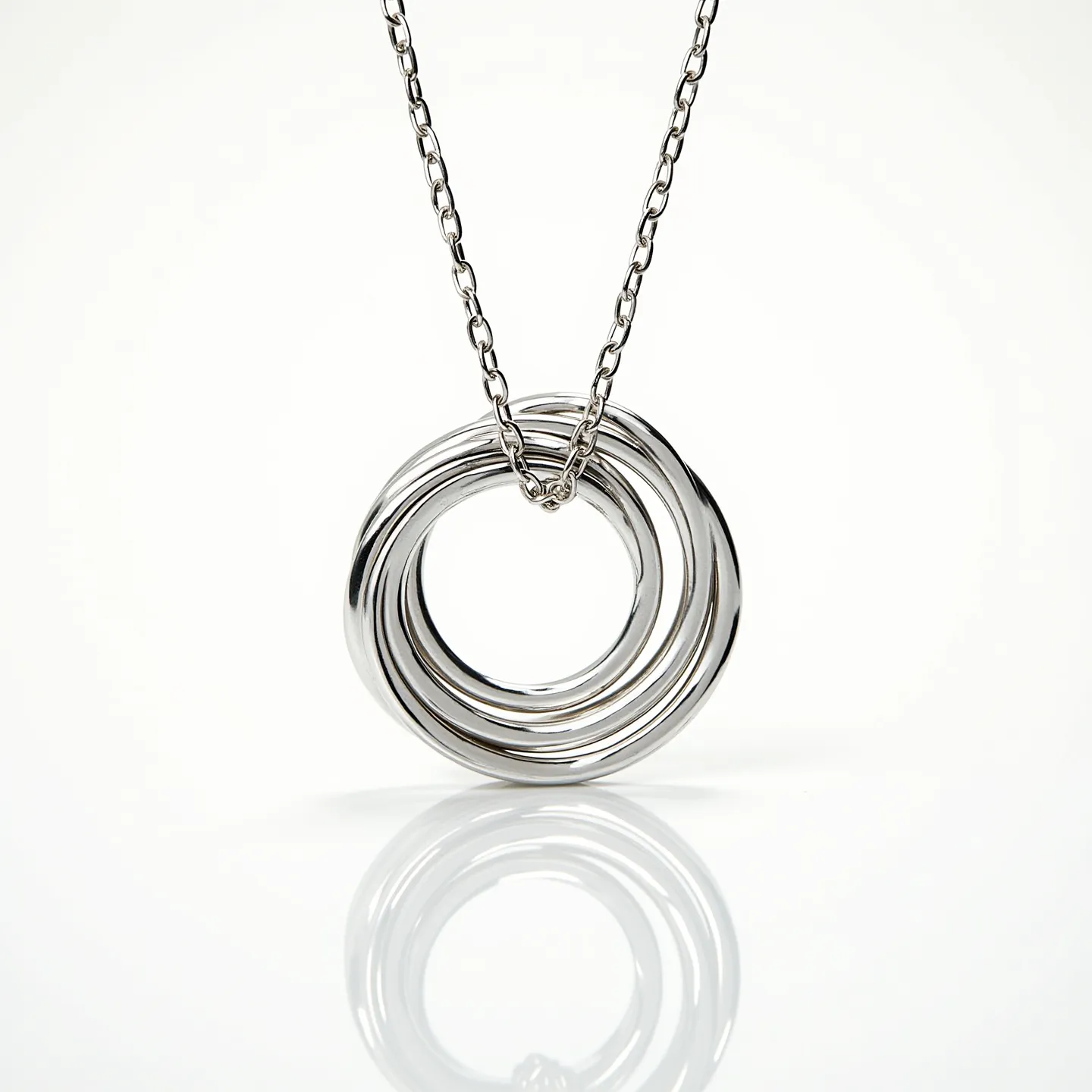 This interlocking circle necklace features a stylish arrangement of multiple polished metal loops, possibly crafted from sterling silver or white gold, given their shiny and smooth finish. The circles are elegantly intertwined to form a unified pendant that hangs from a sleek, matching chain. The necklace appears to use a simple chain link design, creating a seamless transition from the pendant to the chain. There are no visible gems or stones adorning the piece, maintaining a minimalist aesthetic. The clasp or attachment mechanism is not visible in this view, emphasizing the continuous, fluid design of the necklace itself.