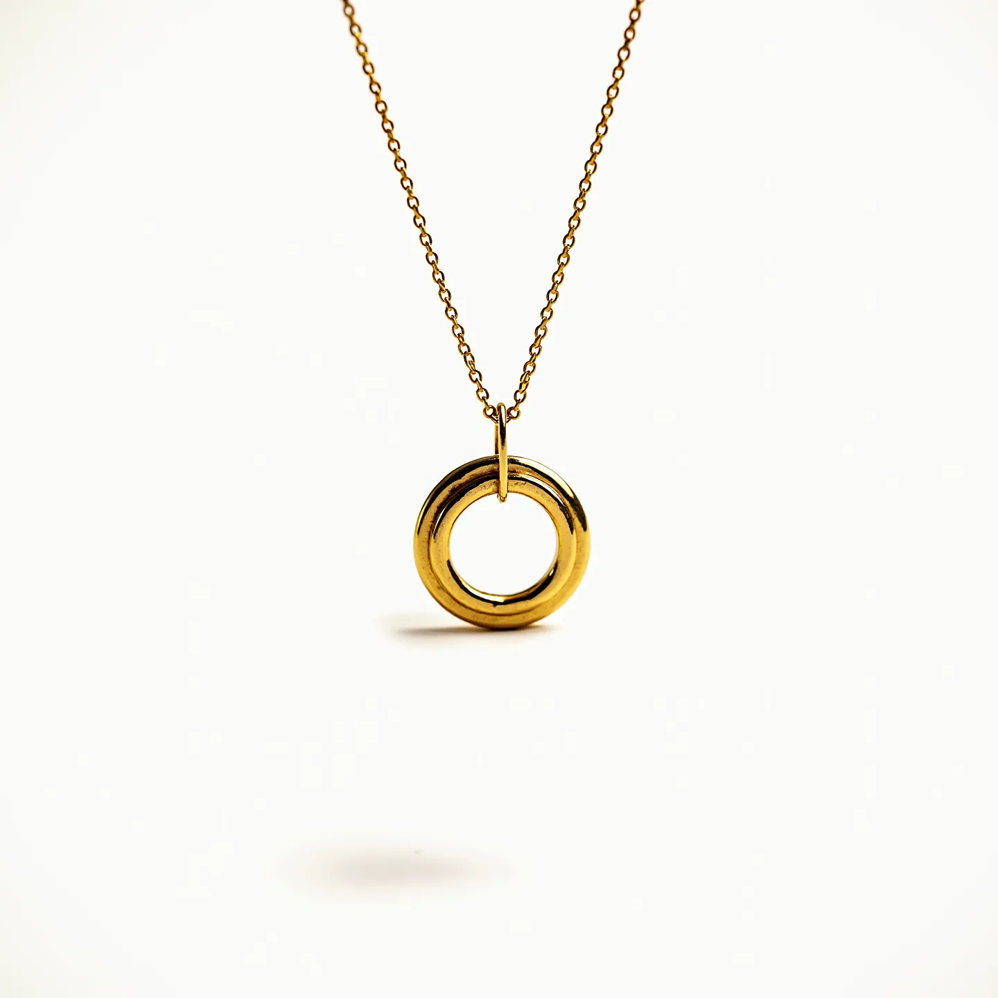 This interlocking circle necklace features a pendant consisting of two intertwined circles, likely made of polished metal with a gold finish, giving it a sleek and elegant appearance. The circles are smoothly rounded, suggestive of a modern and minimalist design. The necklace chain is a delicate link chain, also matching the gold-tone of the pendant, ensuring a cohesive aesthetic. The necklace is designed with a sturdy loop at the top of the pendant connecting it to the chain, allowing for flexible movement.