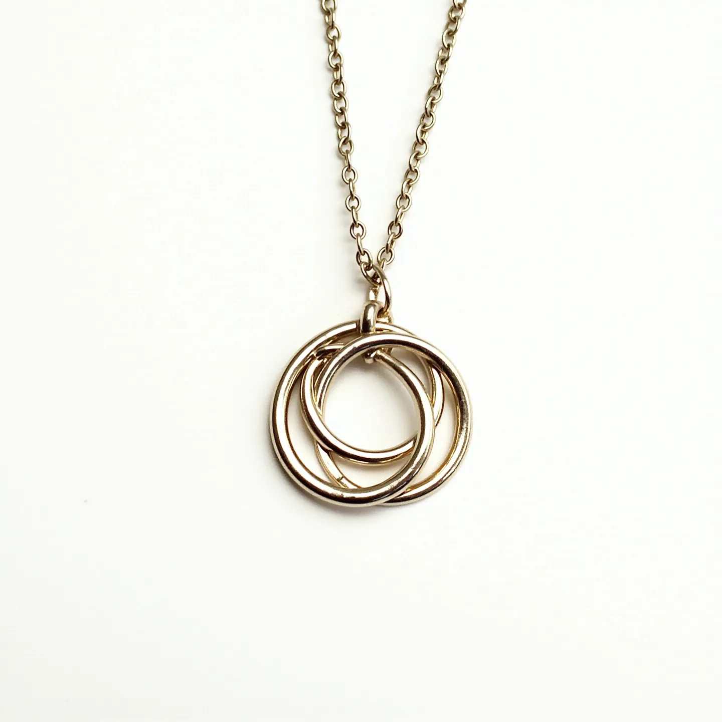 This interlocking circle necklace features a simple and elegant design composed of three intertwined rings. The circles appear to be made of a polished, silver-toned metal, giving them a sleek and modern look. The necklace chain is also made of this matching metal, maintaining a cohesive appearance throughout. The chain has a delicate, rounded link design, which complements the fluidity of the circles. The necklace is designed without any gems or stones, focusing on the minimalist appeal of the interlocking rings. The attachment consists of a standard lobster clasp, ensuring secure closure while wearing.