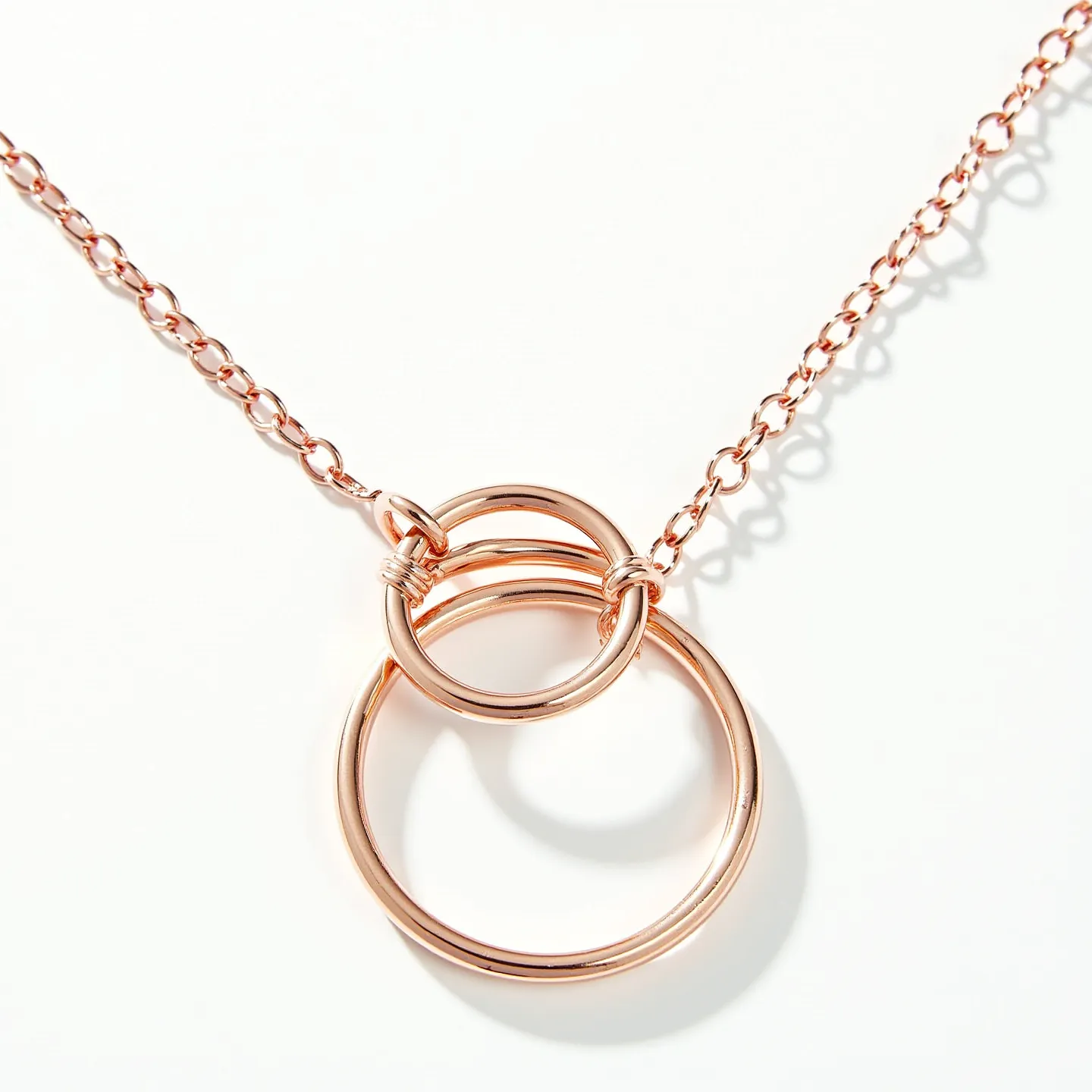 This interlocking circle necklace features a minimalist yet elegant design, composed of two interlocking circles crafted from rose gold-plated metal, which gives it a warm, luxurious tone. Each circle is smooth and polished, accentuating the sleek lines of the design. The necklace is connected with a delicate rose gold chain, which is attached to the circles with small, precise loops. It is likely secured with a standard lobster clasp for ease of wear. This piece embodies a graceful and modern aesthetic, suitable for various occasions.