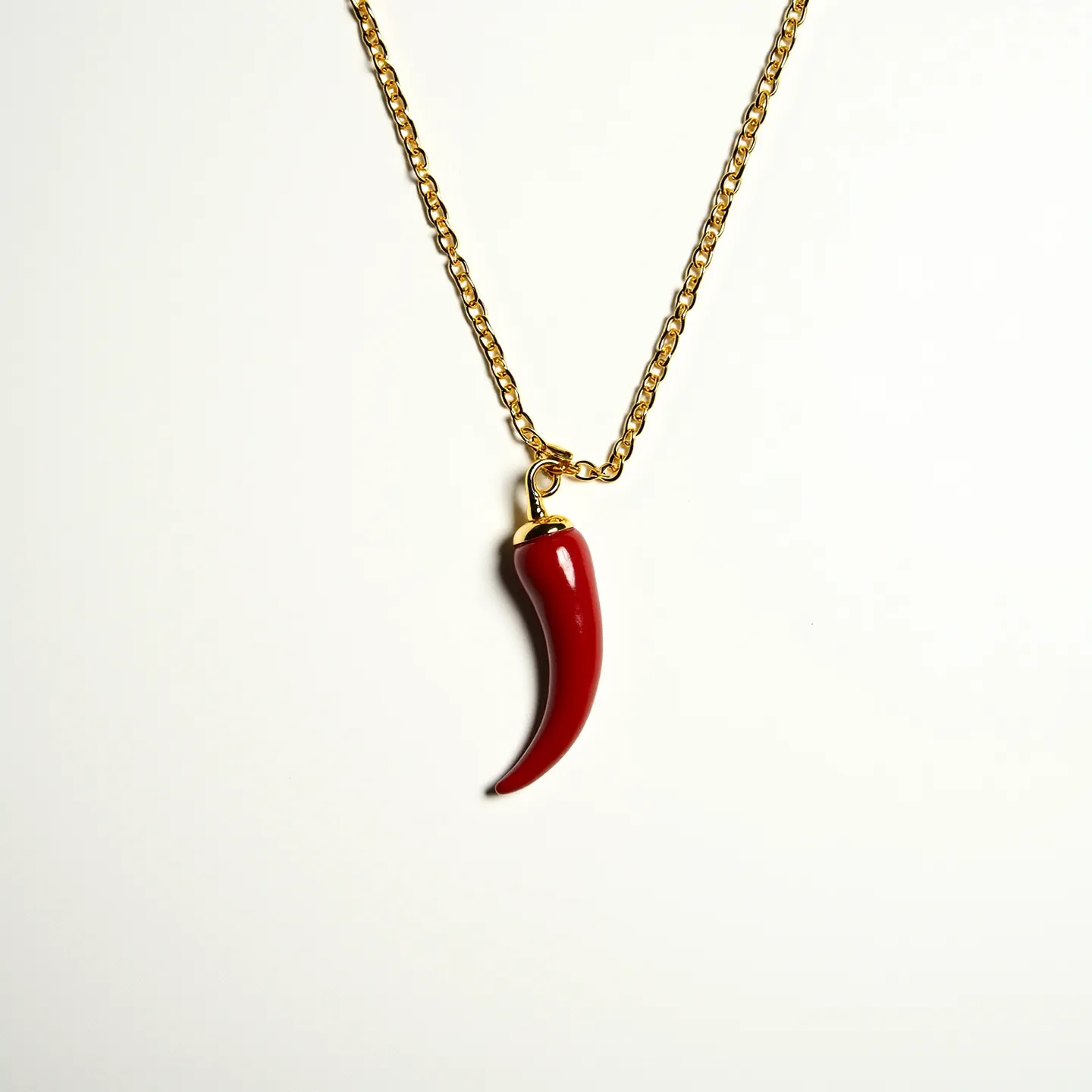 This Italian pepper necklace features a striking red pepper-shaped pendant, likely made from glass or ceramic, that is both smooth and glossy in appearance. The pendant is attached to a gold-toned metal cap which links it to a delicate chain of the same metallic hue, giving the piece a cohesive and elegant look. The chain consists of oval links that complement the pendant's bold red color. This necklace is secured with a standard clasp, ensuring ease of wear while adding to its overall sophistication and charm.