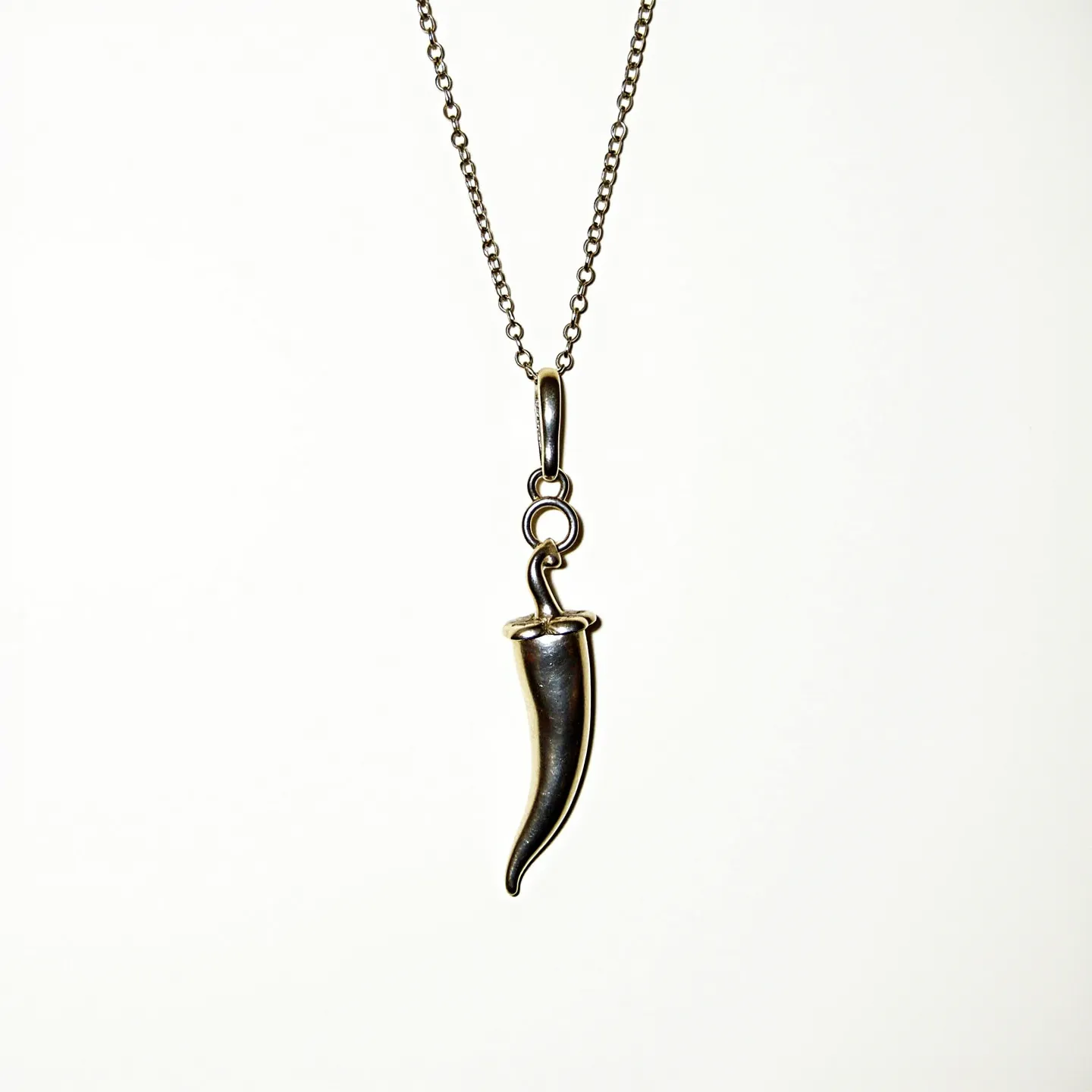 This Italian pepper necklace features a pendant shaped like a chili pepper, crafted from a polished metal, likely silver, which gives it a sleek and shiny appearance. The pendant hangs from a delicate chain comprised of uniformly small links, enhancing the simplicity and elegance of the design. At the top of the pepper, there is a loop connecting to a small ring, which in turn attaches to the main loop on the chain, serving as the attachment mechanism. The necklace does not feature any gemstones or intricate settings, keeping the overall look understated yet stylish.