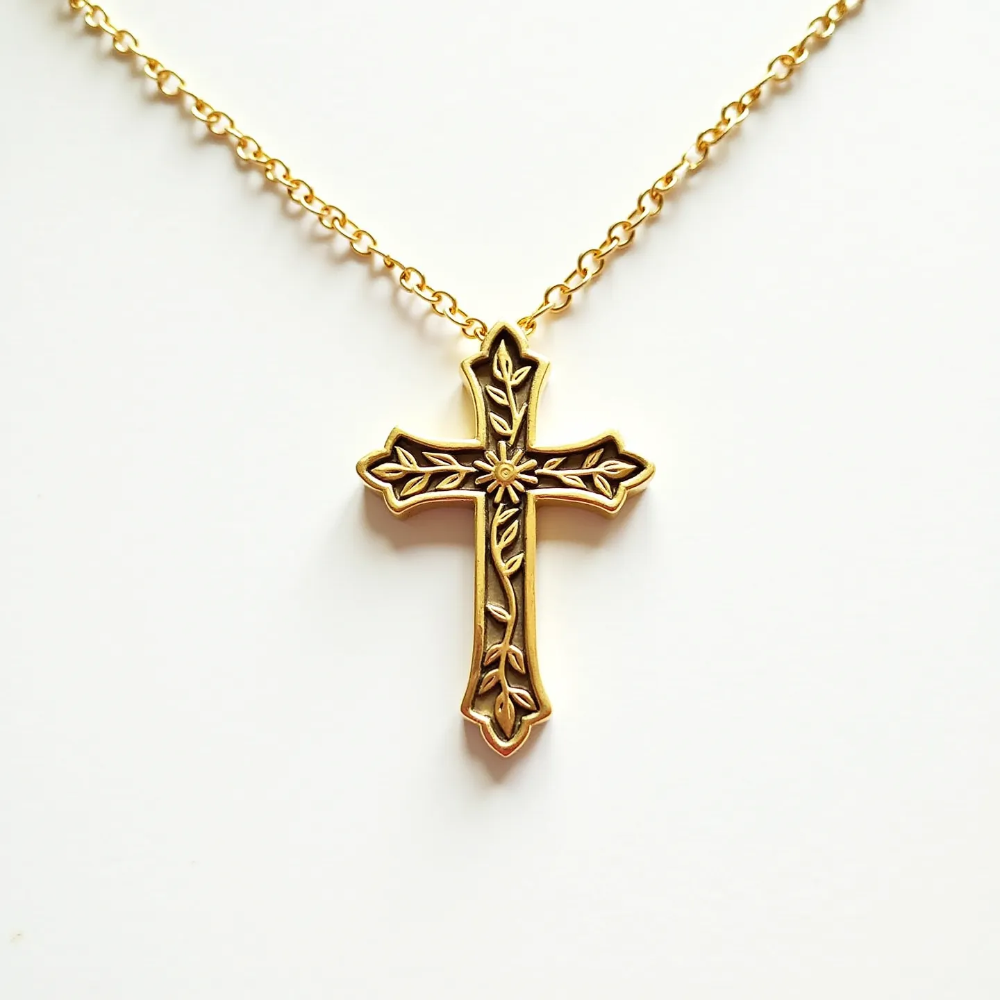 This kids cross necklace features a gold-tone cross pendant adorned with intricate floral and leaf engravings, giving it a delicate and decorative appearance. The cross does not include any gemstones, instead relying on its detailed design for visual interest. It hangs from a matching gold-tone chain that complements the pendant's finish. The chain appears to include a standard clasp mechanism for securing around the neck, ensuring it is suitable for everyday wear. The overall design combines elegance and simplicity, making it an ideal accessory for children.