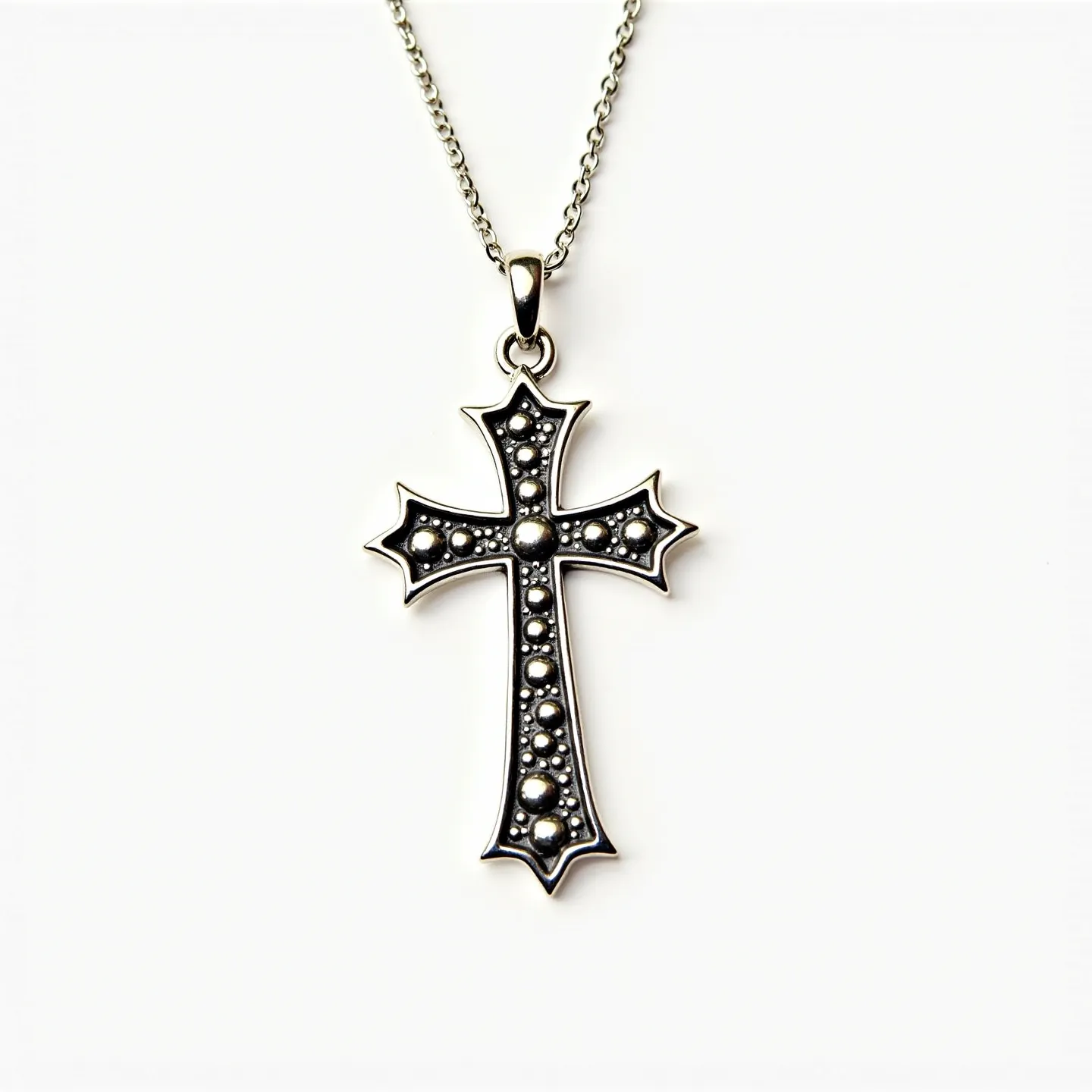 This kids cross necklace features a detailed cross pendant made of metal with a silver-tone finish, adorned with small, round, raised metal dots resembling bezel-set gems. The cross has an intricate design with pointed tips, enhancing its decorative appeal. It hangs from a medium-thickness chain, connected via a simple bail that allows for smooth movement along the chain. The chain features a standard link design, typically closed with a spring ring clasp, ensuring secure wear and easy attachment around a child's neck.