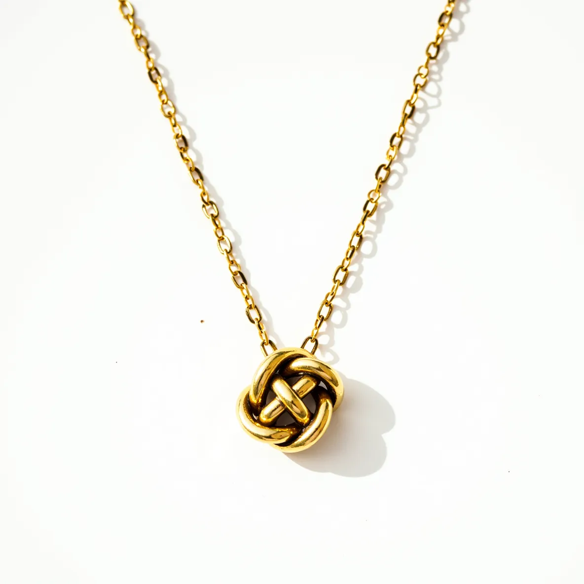 This knot necklace features a delicate design crafted from a gold-toned metal, forming an intricate knot at its center that serves as a striking focal point. The chain is composed of small, uniform links that contribute to the necklace's elegant appearance and ensure a comfortable fit. There are no gemstones embedded within the knot or along the chain, maintaining a minimalist design that highlights the metalwork. The necklace is completed with a clasp that provides secure fastening and easy wearability.