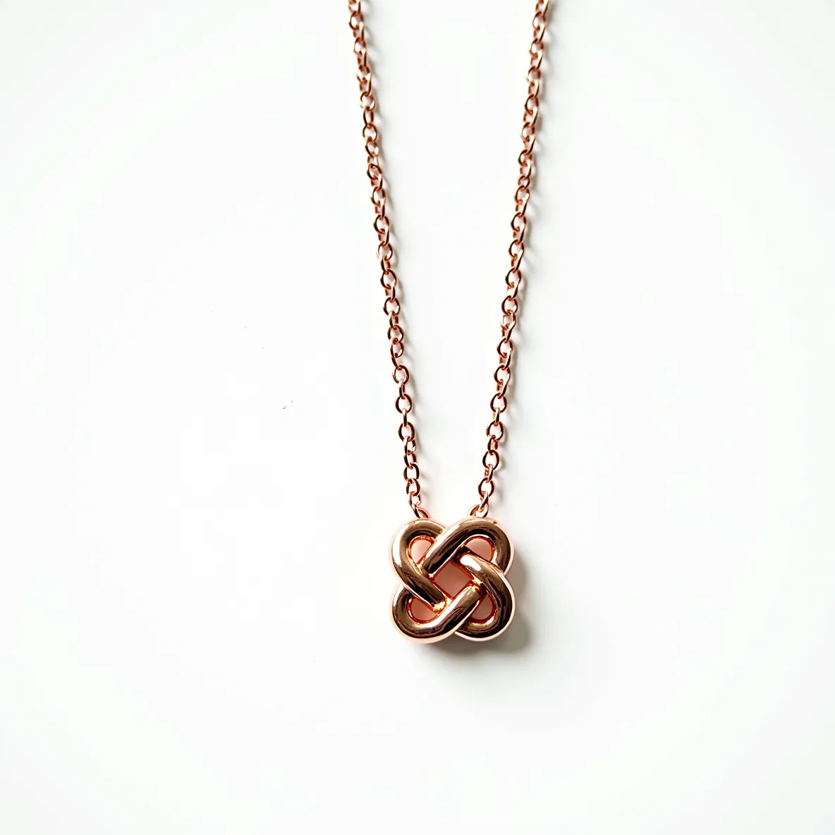 This knot necklace features a lustrous rose gold chain that beautifully complements the intricate knot pendant crafted in the same material. The pendant displays a sophisticated, intertwined loop design, creating a seamless and elegant appearance. The chain is composed of delicately interlinked oval links, offering both durability and a refined aesthetic. The necklace doesn't showcase any gems, which accentuates the simplicity and modernity of the design. It is finished with a traditional clasp that ensures secure and comfortable wear, reflecting a minimalistic yet chic style.