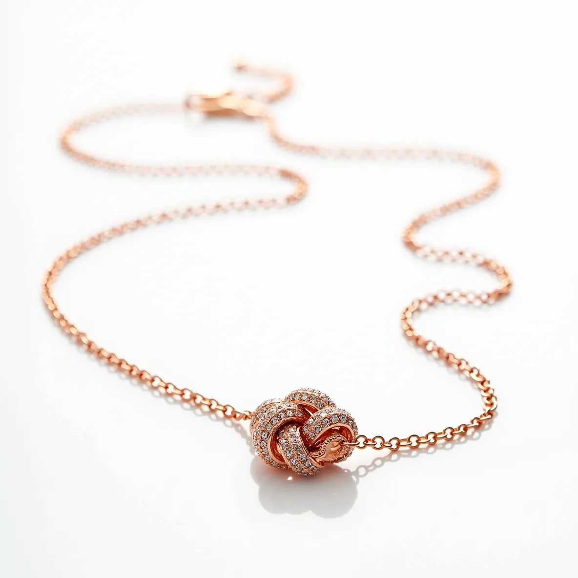 This knot necklace features a delicate and intricate design crafted from a warm, rose gold-toned metal. The central focus of the piece is its knot motif, prominently adorned with sparkling, round-cut diamonds set in a pavé style, adding a touch of elegance and brilliance. The chain is a fine link chain, complementing the sophistication of the overall design. It secures with a lobster clasp, ensuring both style and security. The choice of materials and craftsmanship in this necklace emphasizes both elegance and simplicity, making it a versatile accessory for various occasions.