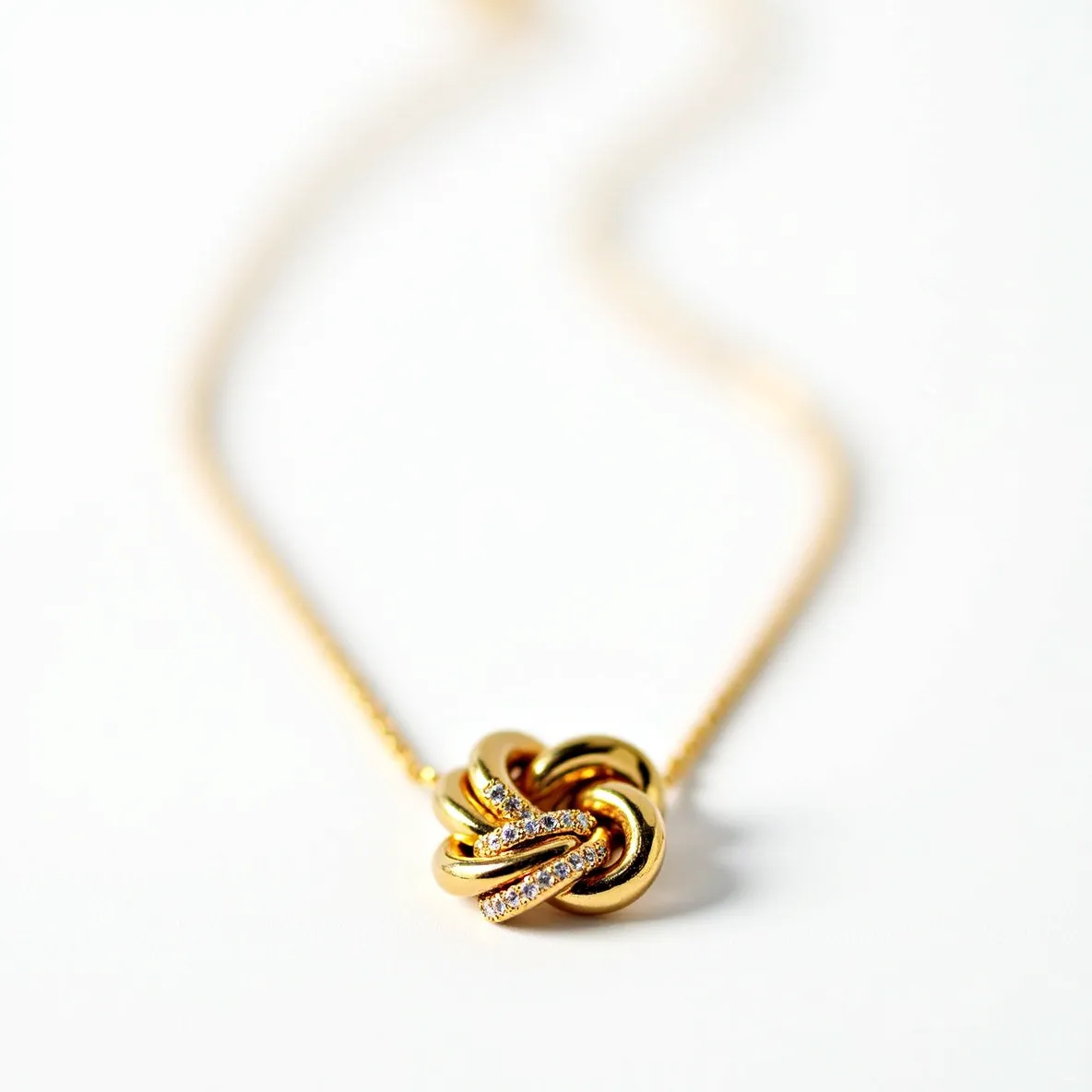 This knot necklace features an elegant and intricate design crafted in polished gold, forming an interwoven knot pattern. Adorning the knot are small, sparkling gemstones, likely diamonds, embedded along selected strands for a subtle shimmer. The diamonds are set in a delicate pave setting, complementing the smooth curves of the gold with a refined and sophisticated touch. The necklace includes a fine gold chain, which seamlessly connects to the knot, suggesting an integrated design. Likely, a standard lobster clasp or similar secure attachment is present, ensuring ease of wear and functionality.