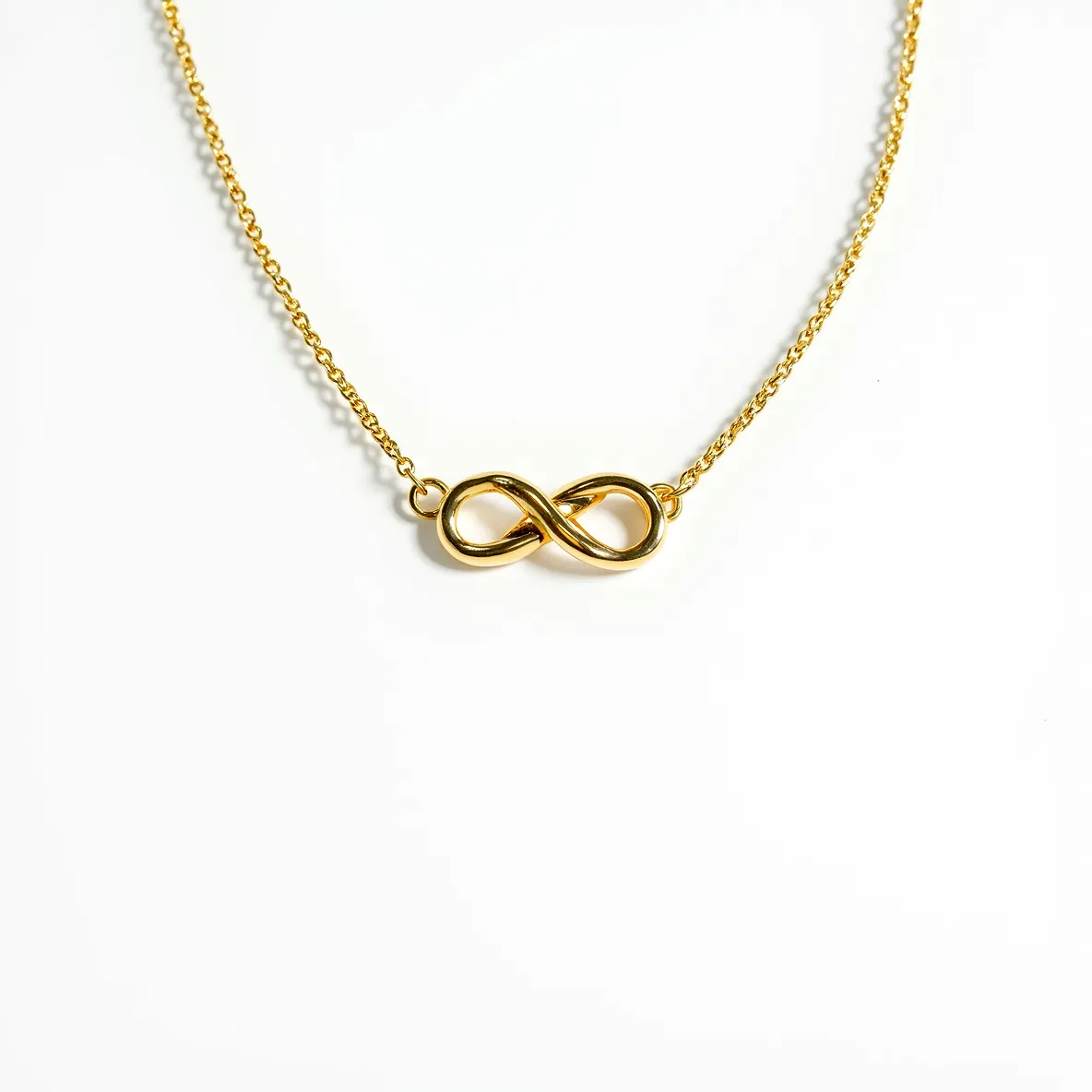 This knot necklace features a beautifully crafted infinity symbol at its center, made from a shiny gold-toned metal. The knot design is sleek and smooth, emphasizing the elegance of the infinity motif. The necklace is accompanied by a delicate chain of the same metallic finish, which complements the central piece seamlessly. The necklace is secured with a simple clasp that maintains the overall minimalist design.