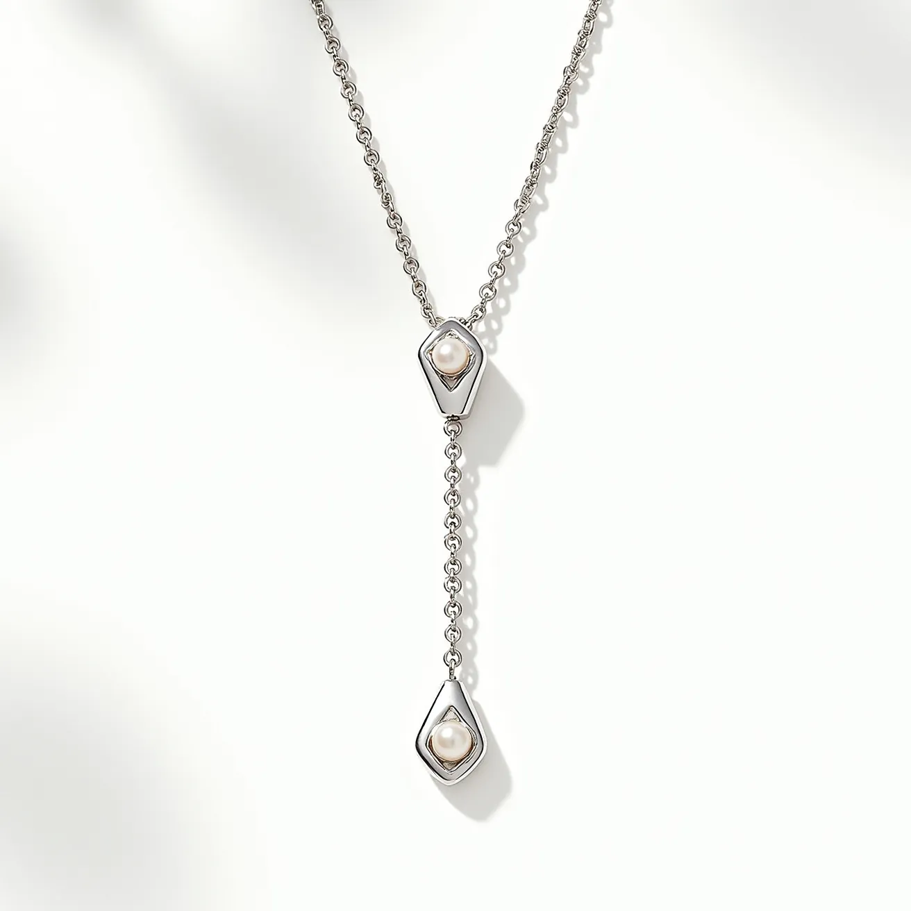 This lariat necklace features a delicate chain crafted from a shiny, silver-toned metal. It showcases two lustrous pearls, each nestled securely within a sleek, geometric setting that adds a contemporary touch to the design. The pearls are highlighted within a teardrop-shaped frame, offering a smooth and elegant contrast against the metallic elements. The necklace's chain flows gracefully into these artistic settings, creating a seamless and sophisticated appearance without the need for a traditional clasp, characteristic of the lariat style.