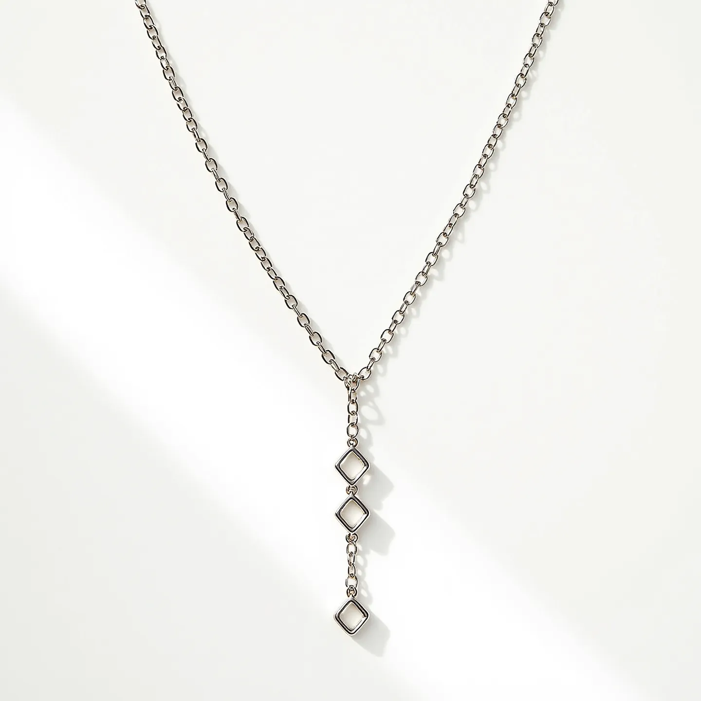 This lariat necklace features a sleek, silver-toned chain that exudes a minimalist elegance. The chain culminates in a vertical drop adorned with three evenly spaced geometric diamond-shaped elements, each serving as focal points. The openwork design of these elements creates an eye-catching interplay of light and shadow. The chain links are uniformly rounded, contributing to the smooth aesthetic and fluid movement of the necklace. The absence of a traditional clasp enhances the seamless, continuous appearance, characteristic of lariat-style pieces, which are designed to be adjustable in length and versatile in style.