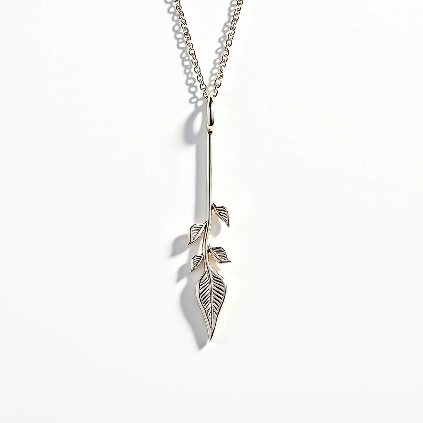 This lariat necklace features a sleek metallic design, evoking a sense of elegance and simplicity. The necklace is composed of a delicate chain, likely crafted from a polished metal such as sterling silver or white gold, contributing to its refined appearance. At the center of the necklace hangs a unique pendant designed in the shape of an elongated leaf with intricately detailed leaf motifs branching off the stem. These details are carefully polished, showcasing expert craftsmanship and adding a touch of sophistication. The design does not incorporate any gemstones, maintaining a minimalist aesthetic focused on the intricate metalwork. The attachment mechanism lacks a traditional clasp, allowing the pendant to loop through the chain, characteristic of a lariat style which emphasizes adjustability and versatility in wear.