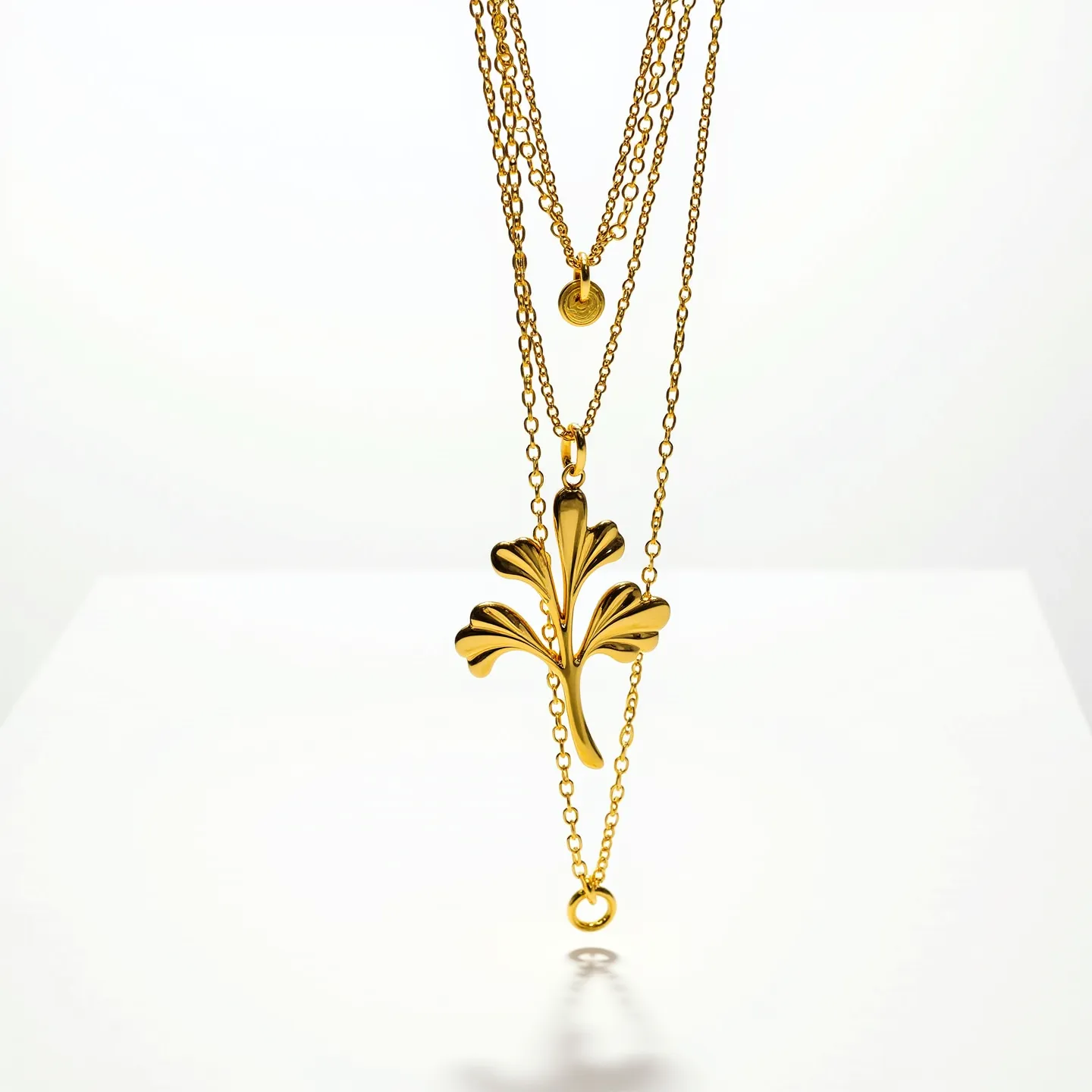 This layered necklace features multiple delicate gold chains that vary in length, creating a cascading effect. The central element is an ornate, gold-toned fleur-de-lis pendant, which draws attention to its elegant design and polished finish. One of the shorter chains includes a simple round disc, adding a subtle touch of detail. The necklace uses a traditional loop clasp, which complements its overall design by providing a secure yet discreet closure.