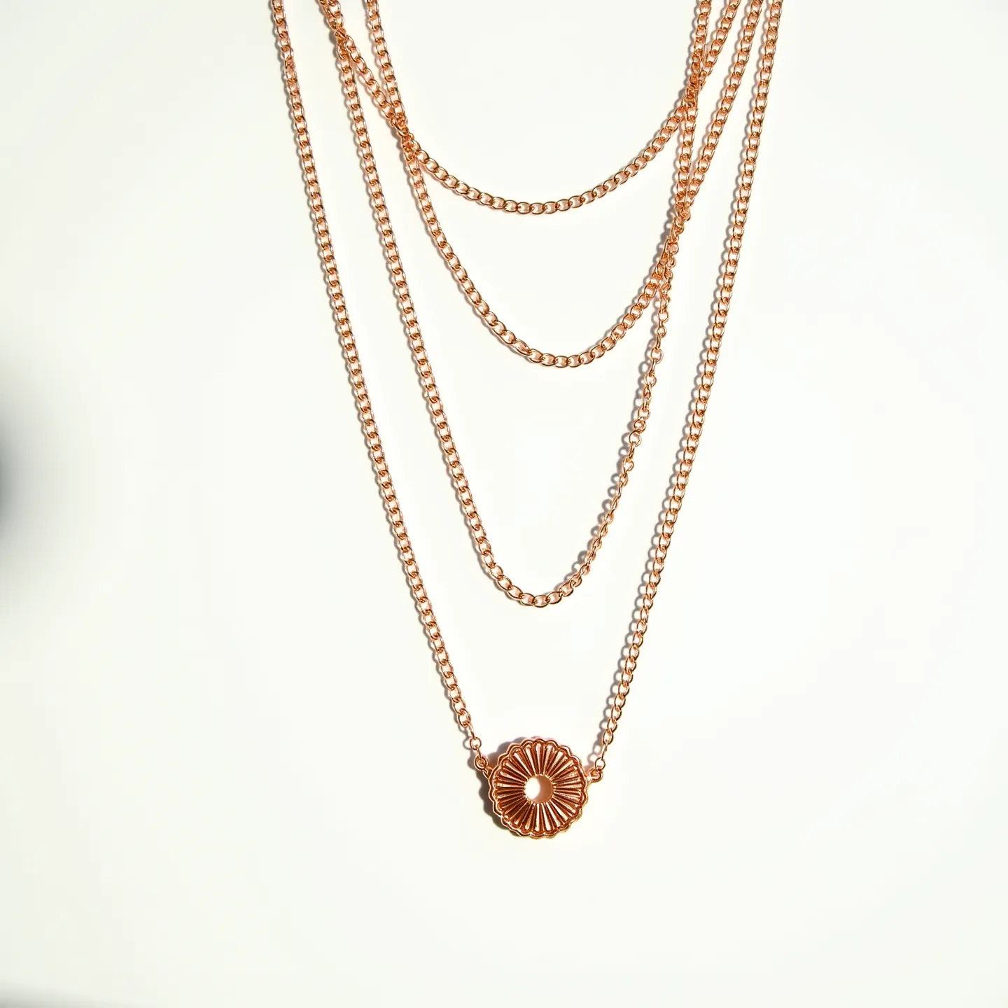 This layered necklace features multiple strands of gold-colored chain, creating a cascading effect. The longest chain has a circular pendant with a sunburst design, highlighting intricate grooves radiating from a central open circle. Each strand adds a sense of depth and dimension to the piece. The necklace is connected by small, round links that provide a delicate and cohesive look. The overall appearance is elegant and versatile, suitable for various styles and occasions.