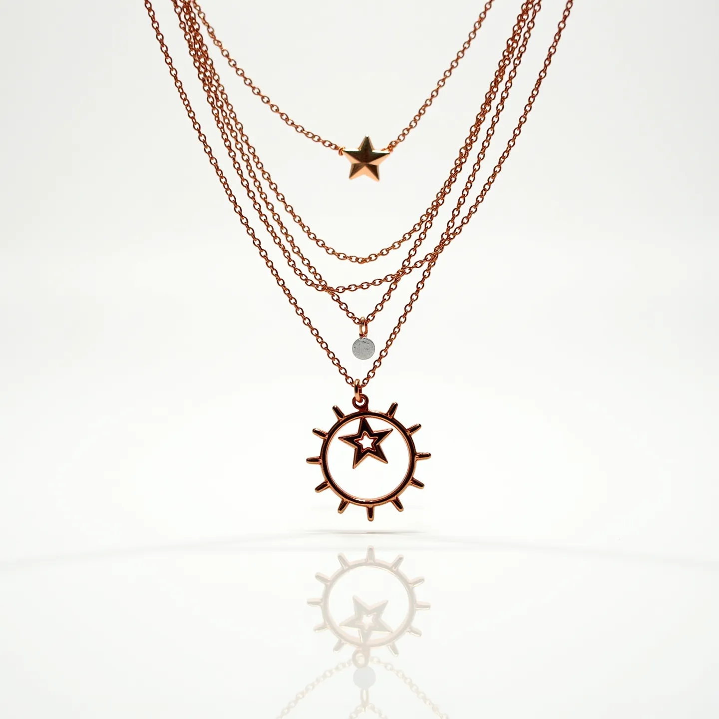 These layered necklace features a series of five delicate chains, each progressively longer to create a tiered effect. The chains appear to be crafted from a rose gold-toned metal, adding a warm and elegant hue to the piece. The first layer showcases a small, raised star charm, while the second layer is adorned with a round bead that resembles a crystal or gemstone, set unadorned in a simple manner. The final, longest layer holds a prominent pendant with a circular sunburst design, enclosing a star cutout. Each element is connected seamlessly to its respective chain, suggesting an integrated attachment without visible clasps interfering with the design's fluidity.