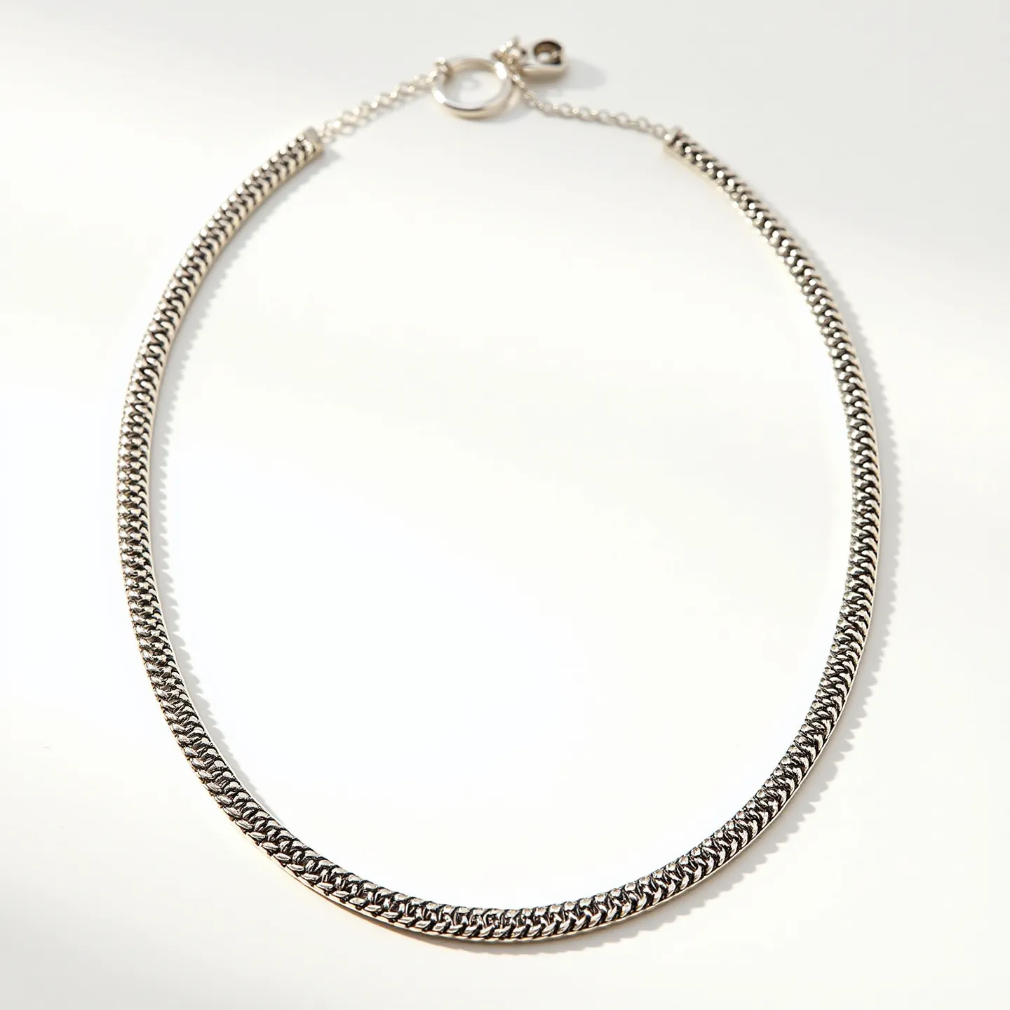 This link necklace is crafted from polished metal with an intricate, woven design that exudes elegance and sophistication. It features a smooth, uniform surface with a subtle sheen, likely due to a high-quality finish. The necklace is devoid of any gemstones, maintaining a classic and minimalist appeal. It is secured with a round lobster clasp that ensures durability and ease of use, complemented by an adjustable chain extension for versatility in fit. The overall construction reveals attention to detail, providing a blend of style and functionality.