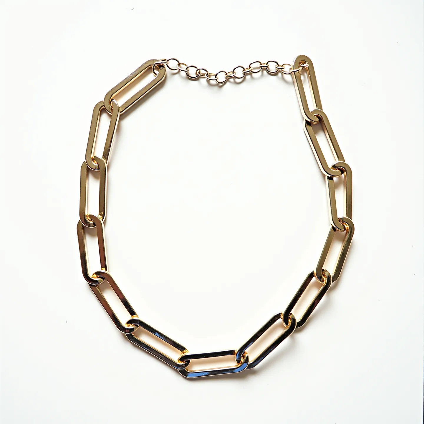 This link necklace features elongated, oval-shaped links with a polished, reflective surface, suggesting it is made of a metal such as gold or gold-plated material. The links connect seamlessly to form a continuous chain, demonstrating a modern and elegant design. It incorporates a small extension chain at the end with a simple lobster clasp, allowing for adjustable length and secure closure. The sleek, classic design makes it versatile for various styles and occasions.