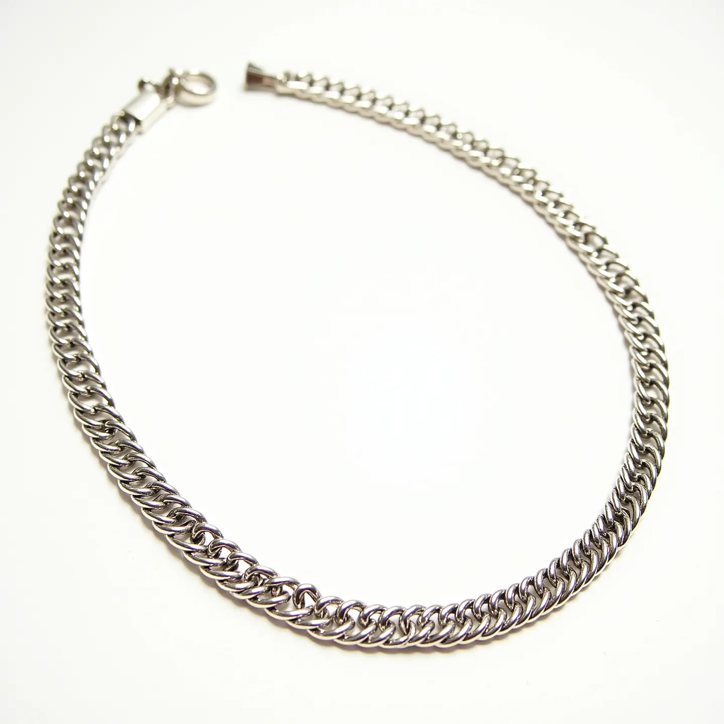 This link necklace features a sleek and polished silver tone, composed of interlocking curb-style links that create a fluid and elegant appearance. The links are uniform in size, lending a consistent and classic look to the piece. It is equipped with a durable spring ring clasp, ensuring secure wear while maintaining an understated design. The necklace does not showcase any additional embellishments such as gems or stones, focusing on the simplicity and sophistication of the metalwork itself.