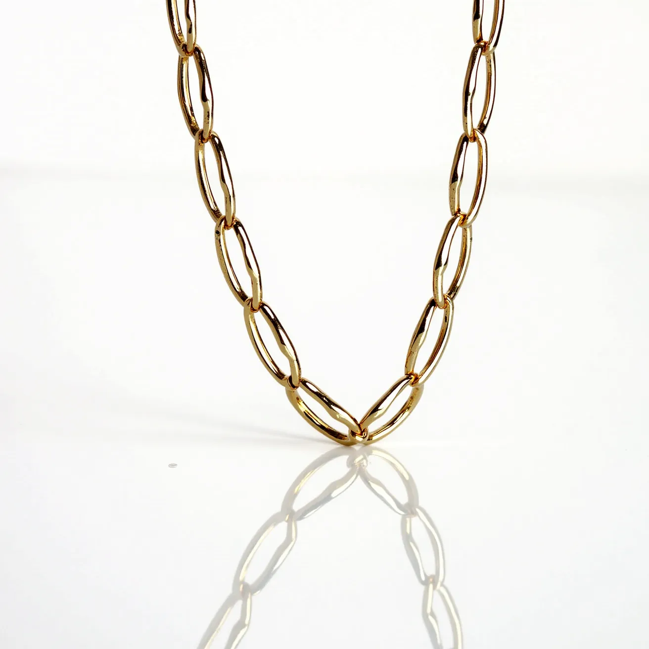 This link necklace features elongated, oval-shaped links crafted from a polished gold metal, providing a sleek and sophisticated appearance. The links are uniform in size, creating a consistent visual flow throughout the design. Due to the simplicity and elegance of the links, the necklace likely uses a lobster clasp for secure fastening, although it is not visible in this view. This necklace exudes timeless charm, ideal for both casual and formal occasions.