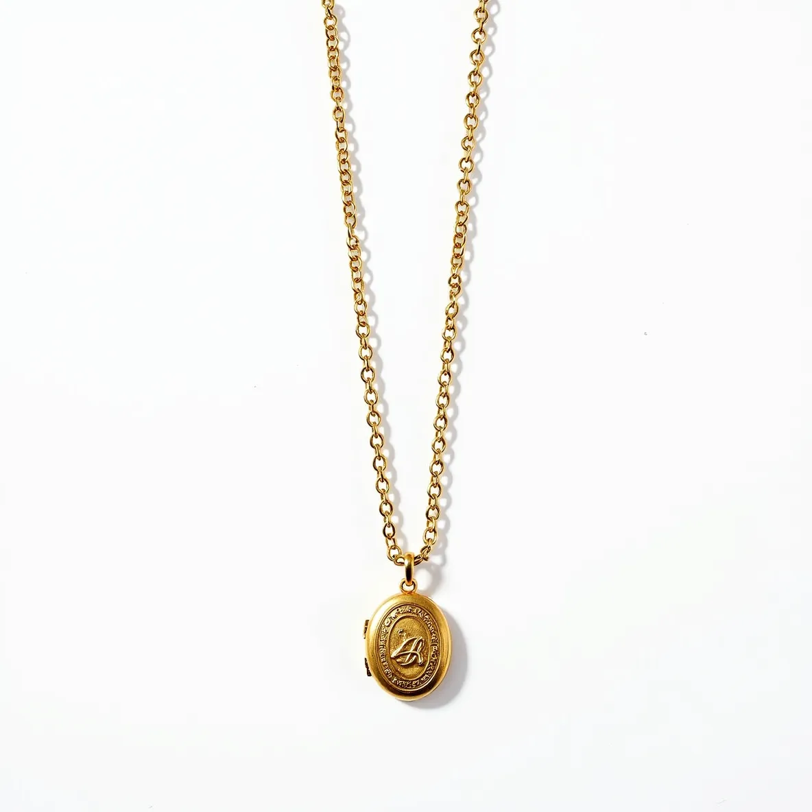 This locket necklace features a gold-tone oval pendant with intricate detailing on its surface, showcasing an engraved monogram or motif within a decorative border. The chain is composed of small, uniform links that complement the classic style of the locket. The clasp appears to be of a standard design, ensuring secure fastening. The overall design suggests a timeless, elegant piece that combines both functionality and ornamental appeal without any additional gems or stones.