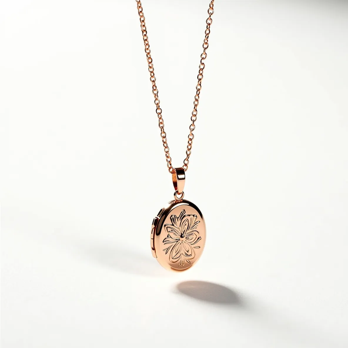 This locket necklace features a delicate, rose gold chain that complements the warmth of the matching locket. The oval-shaped locket showcases an intricately engraved floral design on its polished surface, adding an elegant touch. The locket is attached to the chain with a sleek bail, ensuring it hangs securely. The chain has a simple, classic cable link style, which pairs well with the overall timeless aesthetic of the piece.