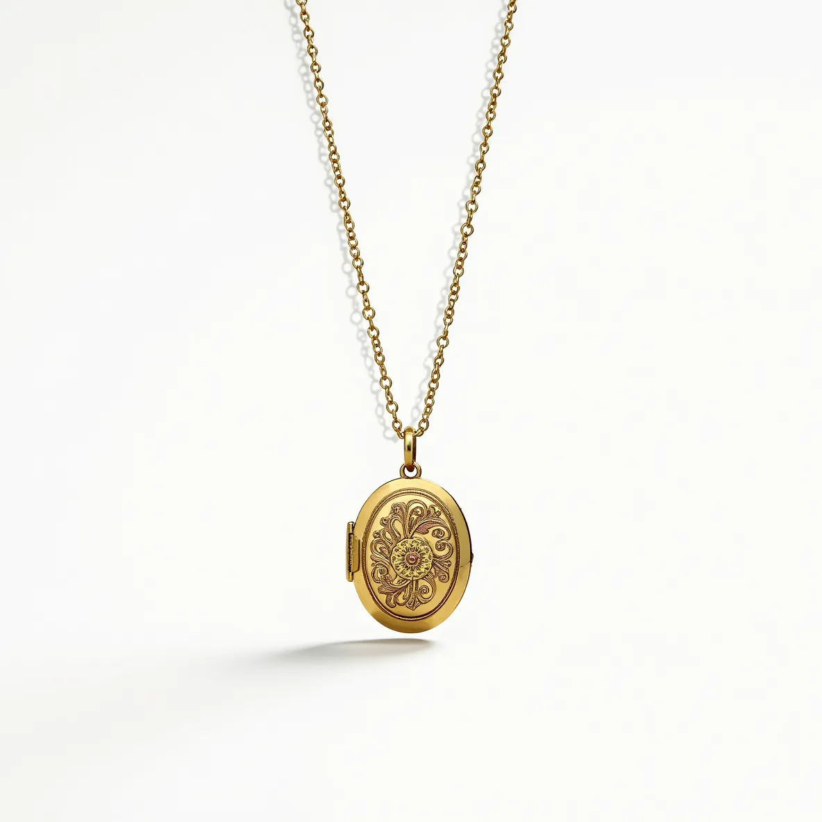 This locket necklace features a delicate gold chain with small, evenly spaced links that add an elegant touch to its overall design. The pendant is an oval-shaped locket, crafted from gold-toned metal, showcasing an intricate floral pattern engraved on its front. At the center of the design, there is a small, round gemstone that appears to be a ruby, set flush within the metal, adding a subtle pop of color. The locket is attached to the chain with a small loop, allowing for smooth movement, and is secured with a discreet, functional clasp, ensuring it stays safely fastened when worn.