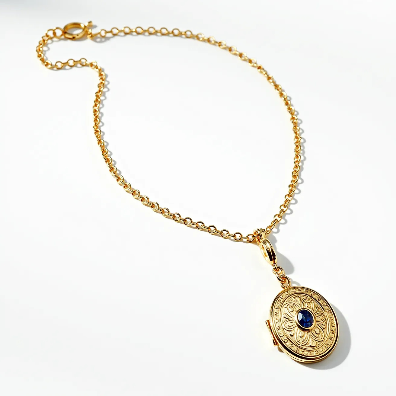 This locket necklace features a gold chain with a round link design, elegantly holding a beautifully crafted oval-shaped locket. The locket is adorned with intricate engravings and showcases a central blue gemstone, likely a sapphire, set in a bezel setting, adding a touch of sophistication. The gem appears to have an oval cut, complementing the overall design of the locket. The necklace is equipped with a spring ring clasp, ensuring secure and easy wearability. The gold hue of the necklace enhances the richness of the design, making it a classic accessory for any jewelry collection.