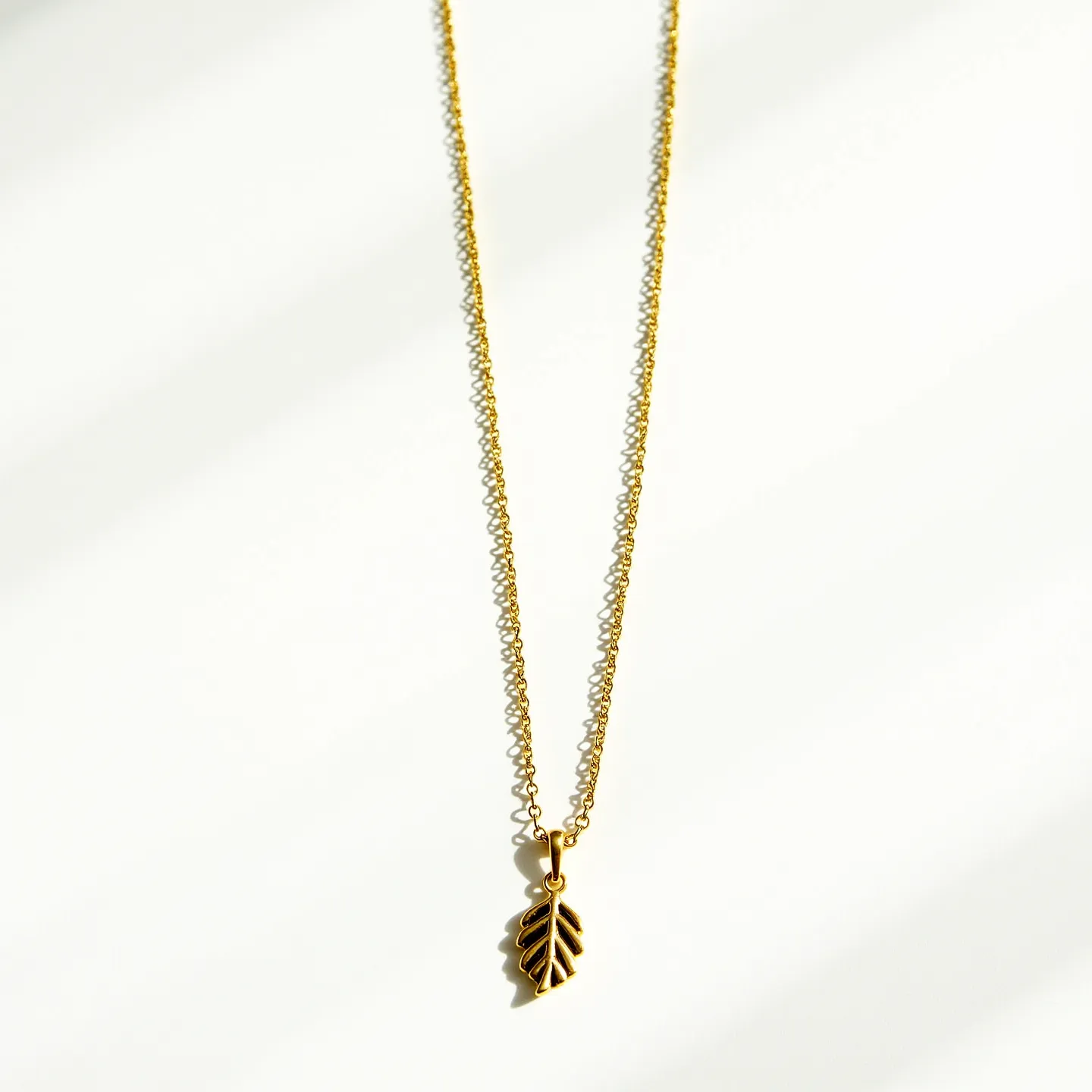 This long gold necklace features a delicate and finely linked chain that holds a charming gold leaf pendant. The pendant is crafted in the shape of an intricately designed leaf, showcasing detailed veining that adds a touch of elegance. The pendant is attached to the chain with a small gold loop, ensuring it hangs gracefully. The necklace appears designed for a simple clasp, offering ease of wear. The entire piece embodies a sleek and minimalist aesthetic, highlighting its beautiful craftsmanship.